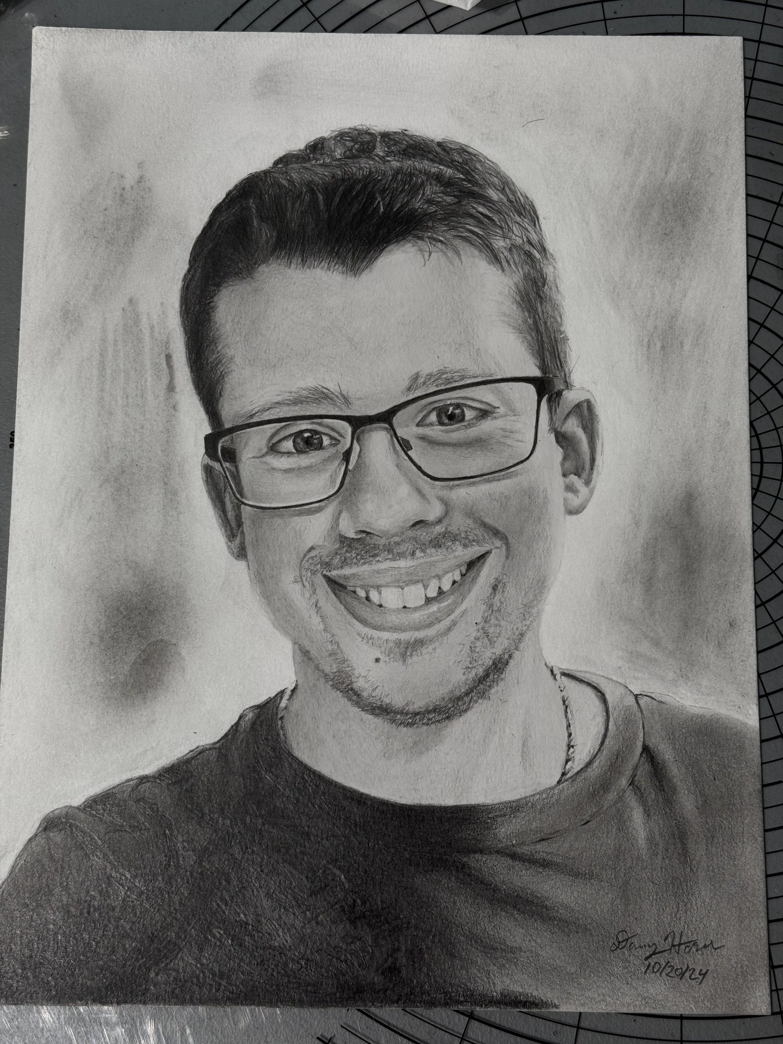 Hand-drawn portrait of a smiling man with glasses, short curly hair, and a beard, signed by the artist and dated 10/2024.