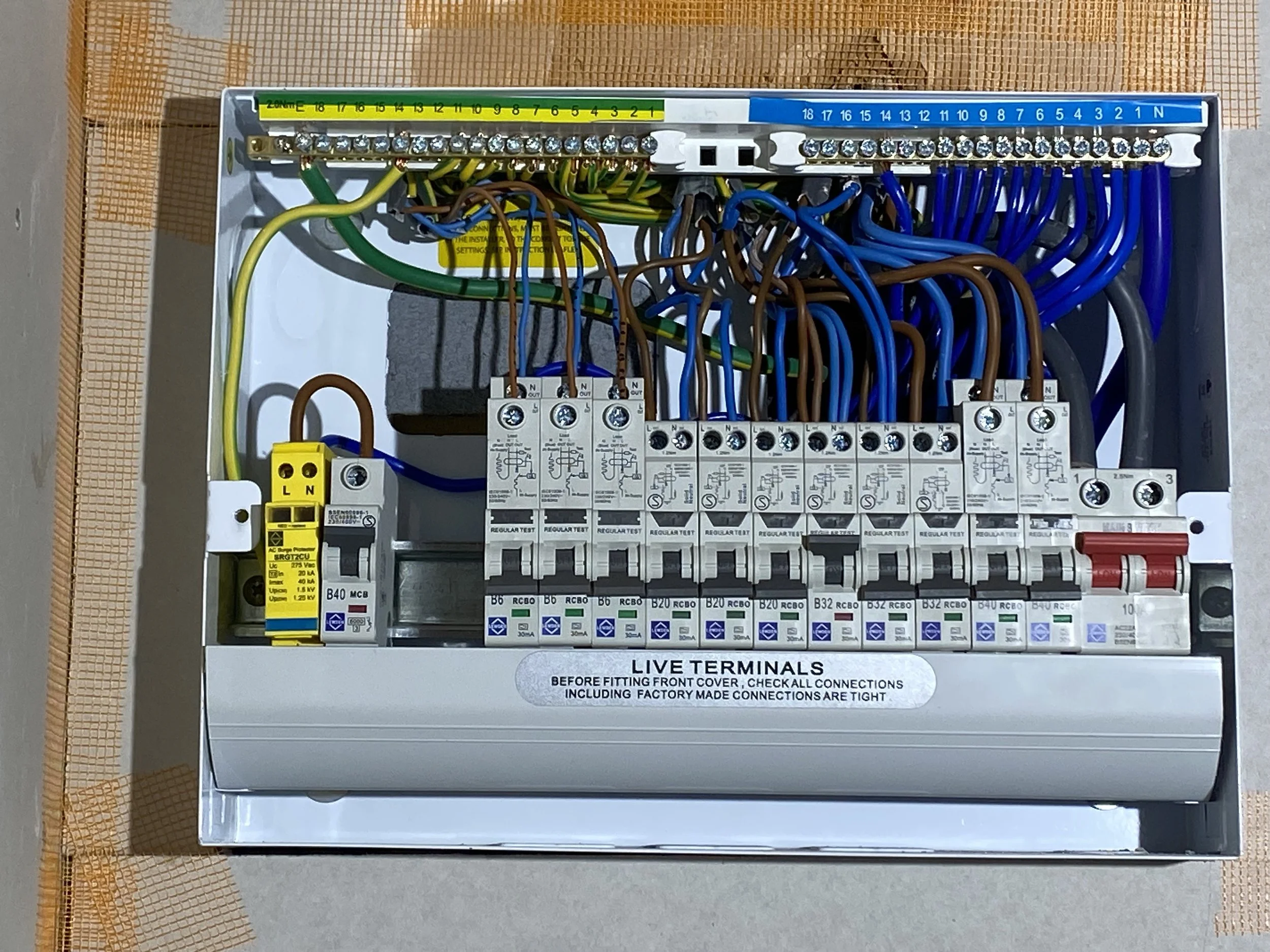 An electrical control panel with multiple circuit breakers and wiring, mounted inside an electrical box labeled 'LIVE TERMINALS' with instructions for installation.