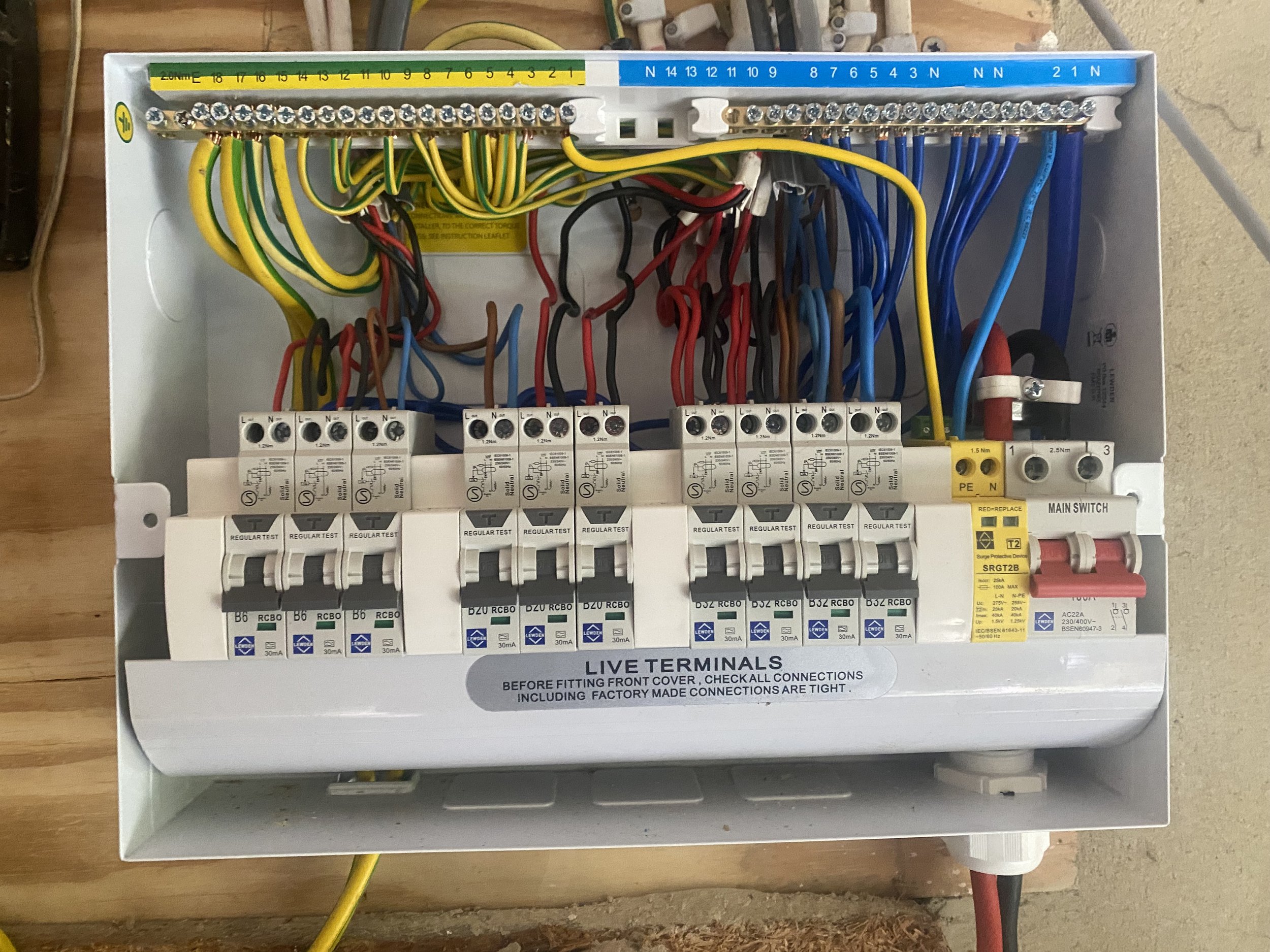 Electrical control panel with live terminals and circuit breakers, wiring, and labels. The panel is mounted in a white box with text indicating it is for live terminals and includes instructions to check connections before fitting the cover.