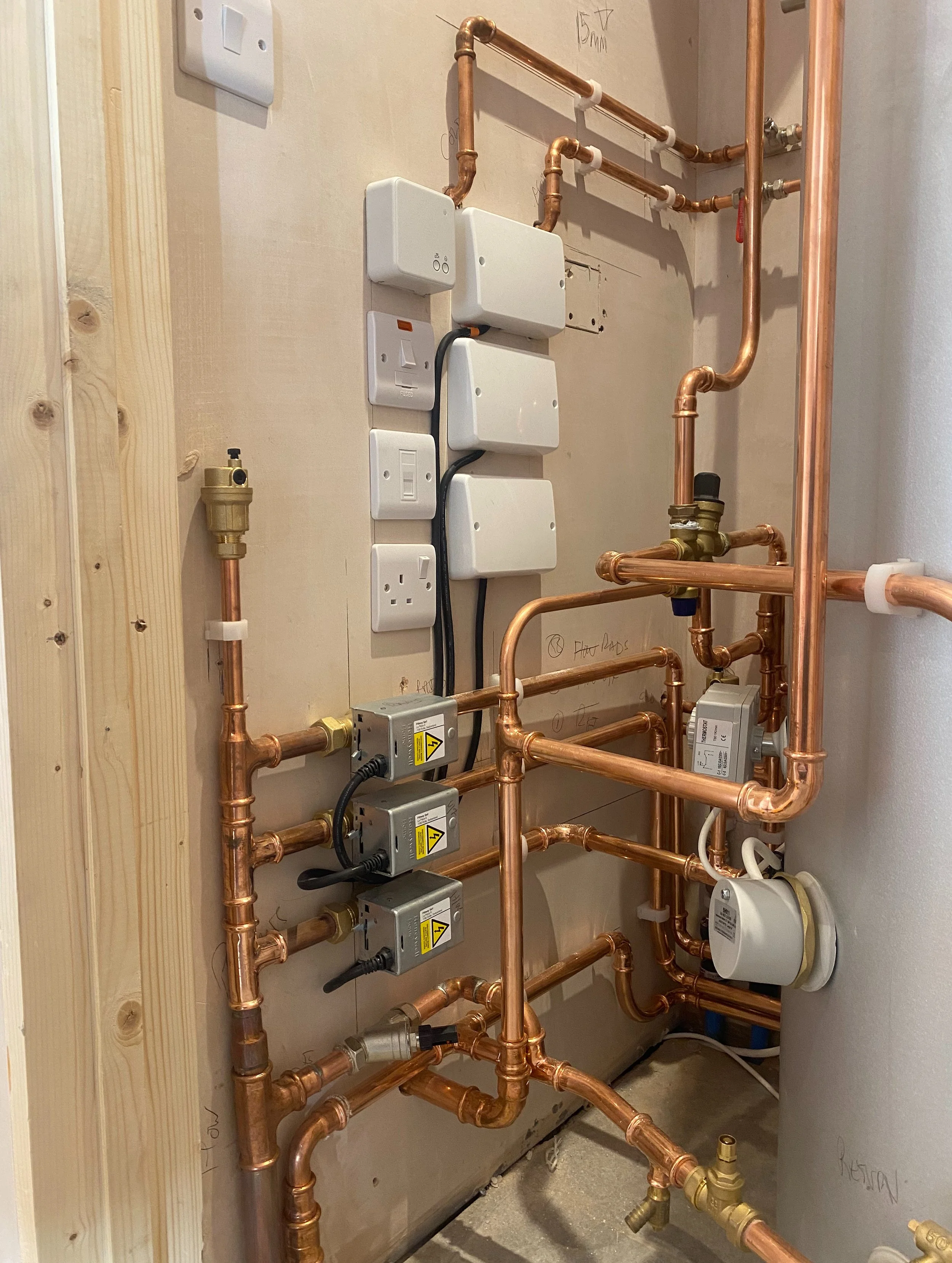 Photo of copper pipes, electrical boxes, and electrical outlets installed on a wall in a building utility or mechanical room.
