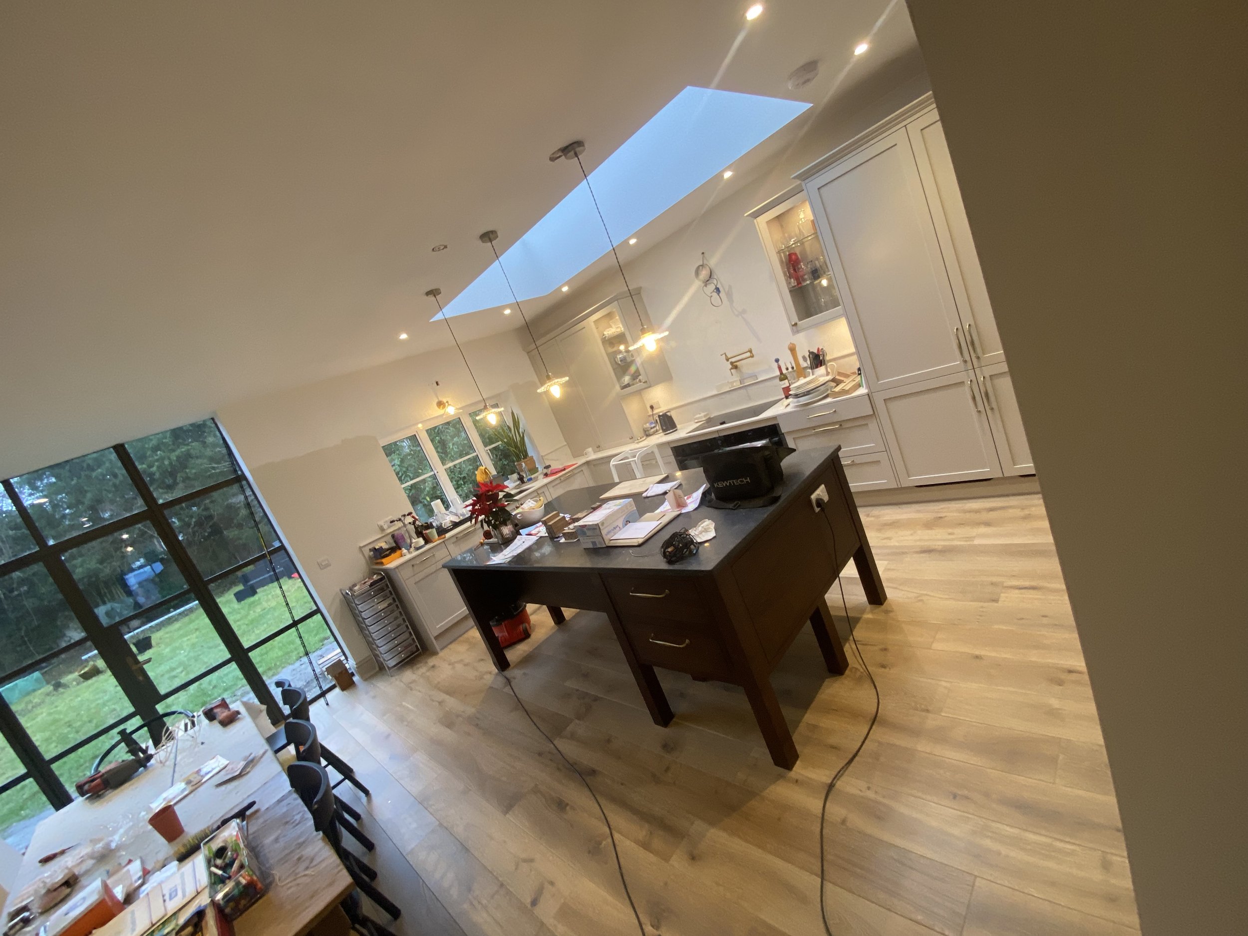 A kitchen with white cabinets, a dark kitchen island, and a skylight on the ceiling. There is a dining table with chairs and a large window showing an outdoor scene.