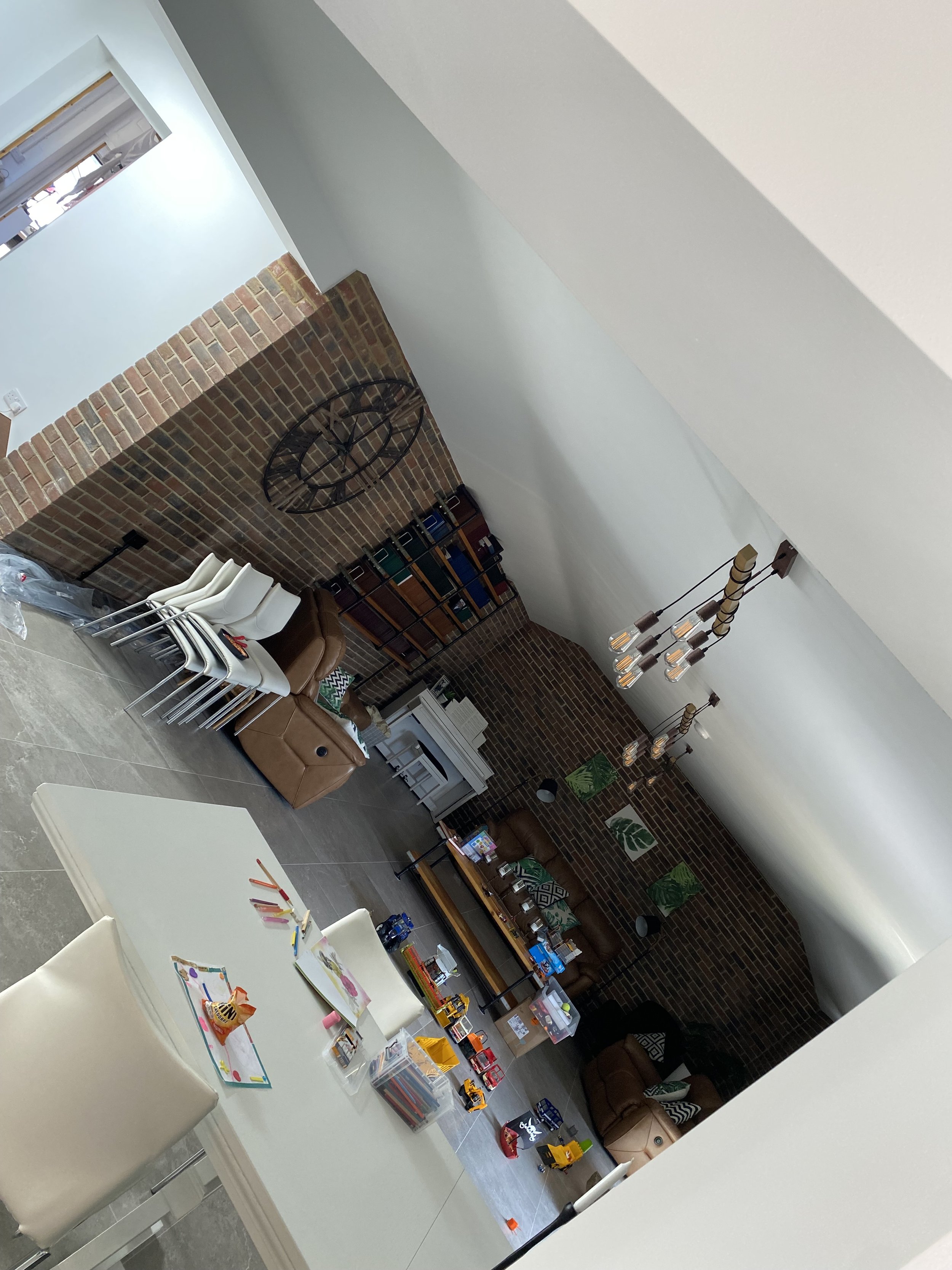 Interior of a modern living room with brick walls, a large clock, bookshelves, and a table with children's toys and drawings.