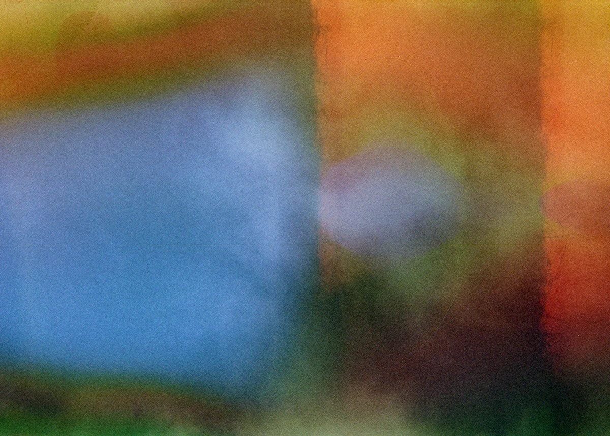 The image appears to be an abstract, blurry photo with various colors including green, blue, red, and yellow, with no distinct objects or scene visible.