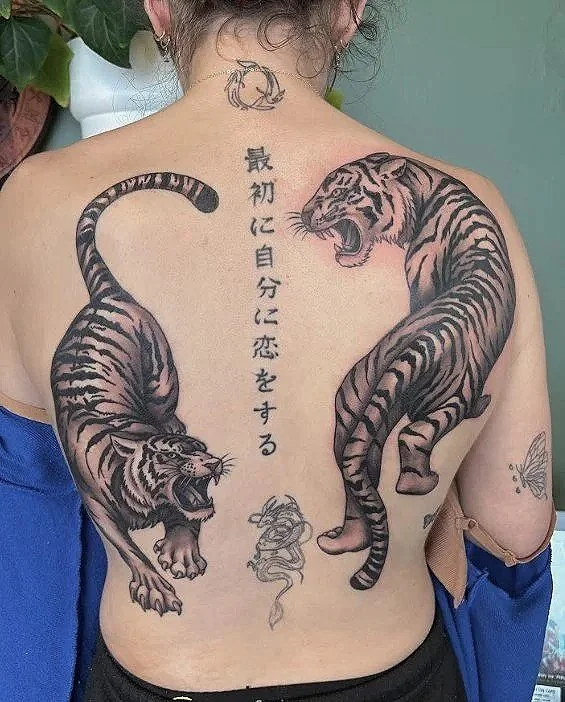 Back tattoo of two fierce tigers facing each other, with Japanese characters in the center and a small snake at the top.