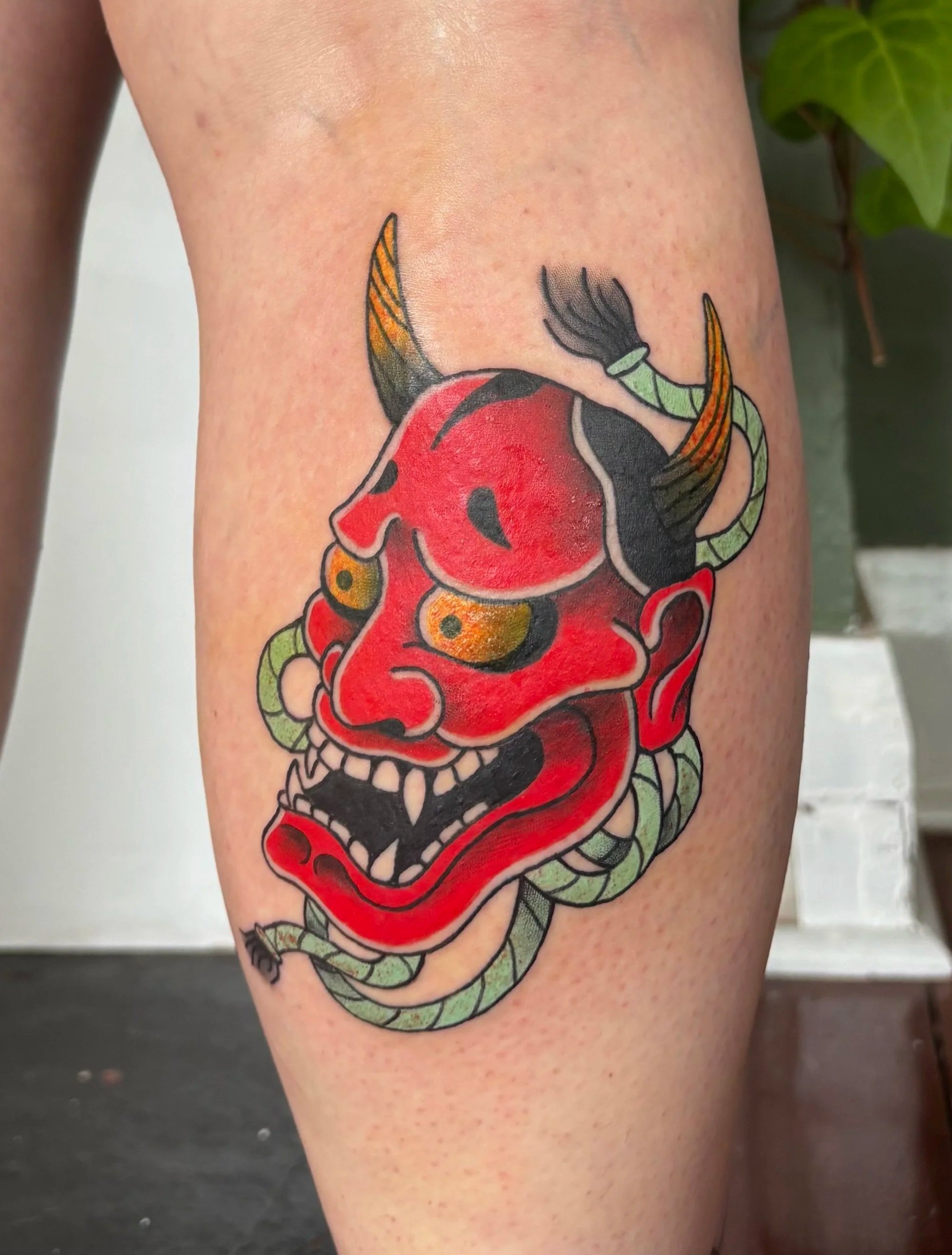 Colorful tattoo of a demon skull with horns on a person's upper arm.
