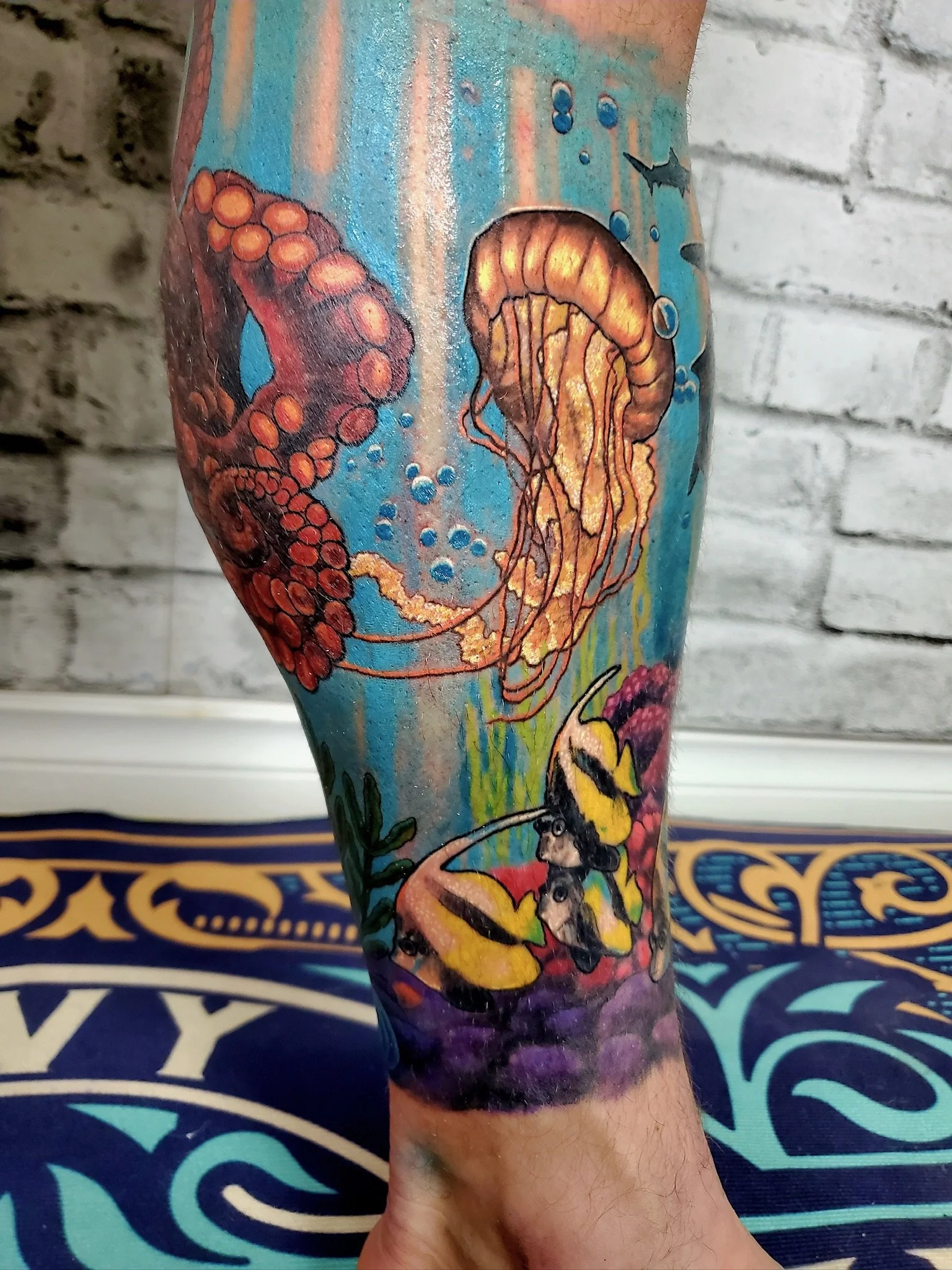 Tattoo of an underwater scene with an octopus, a jellyfish, and a fish, set against a blue background with bubbles and water effects.