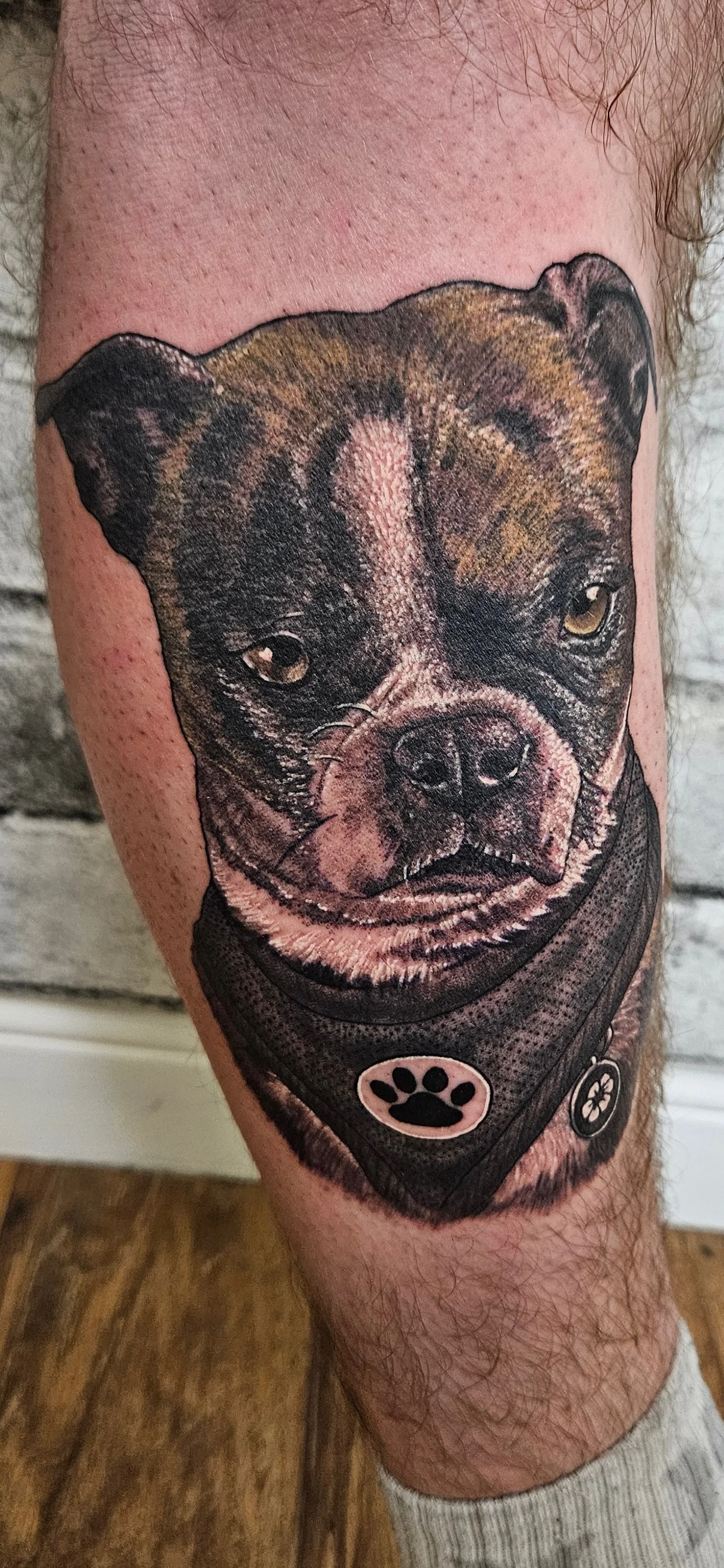 Photo realistic tattoo of a dog wearing a bandana on a person's leg.