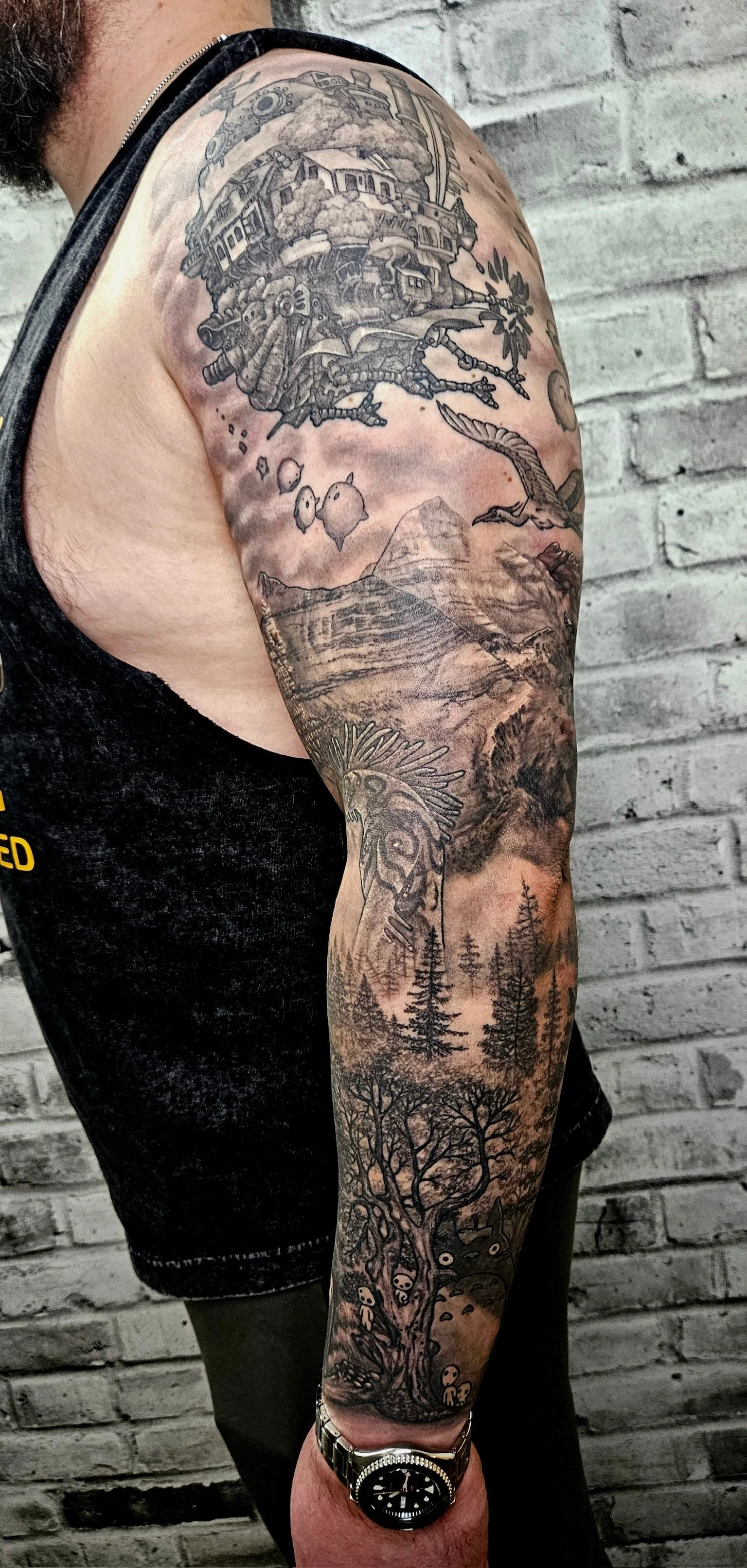 Tattoo sleeve featuring a detailed landscape scene with mountains, a tree in the foreground, flying birds, a dragon, and various other elements, all in black and gray ink.