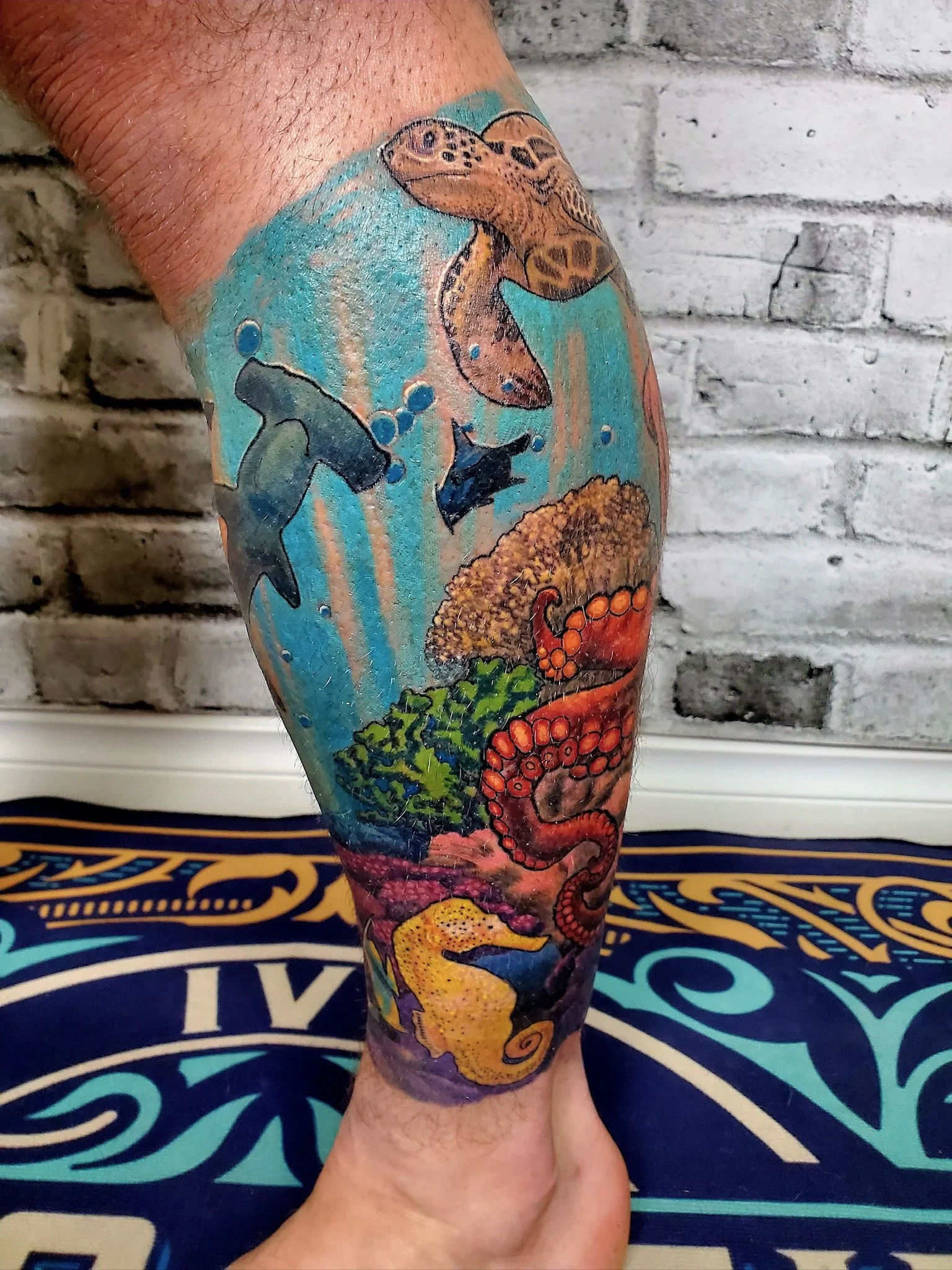 A detailed colorful tattoo sleeve on a person's arm featuring various marine life and abstract designs, including a large octopus, a fish, coral, and ocean waves.