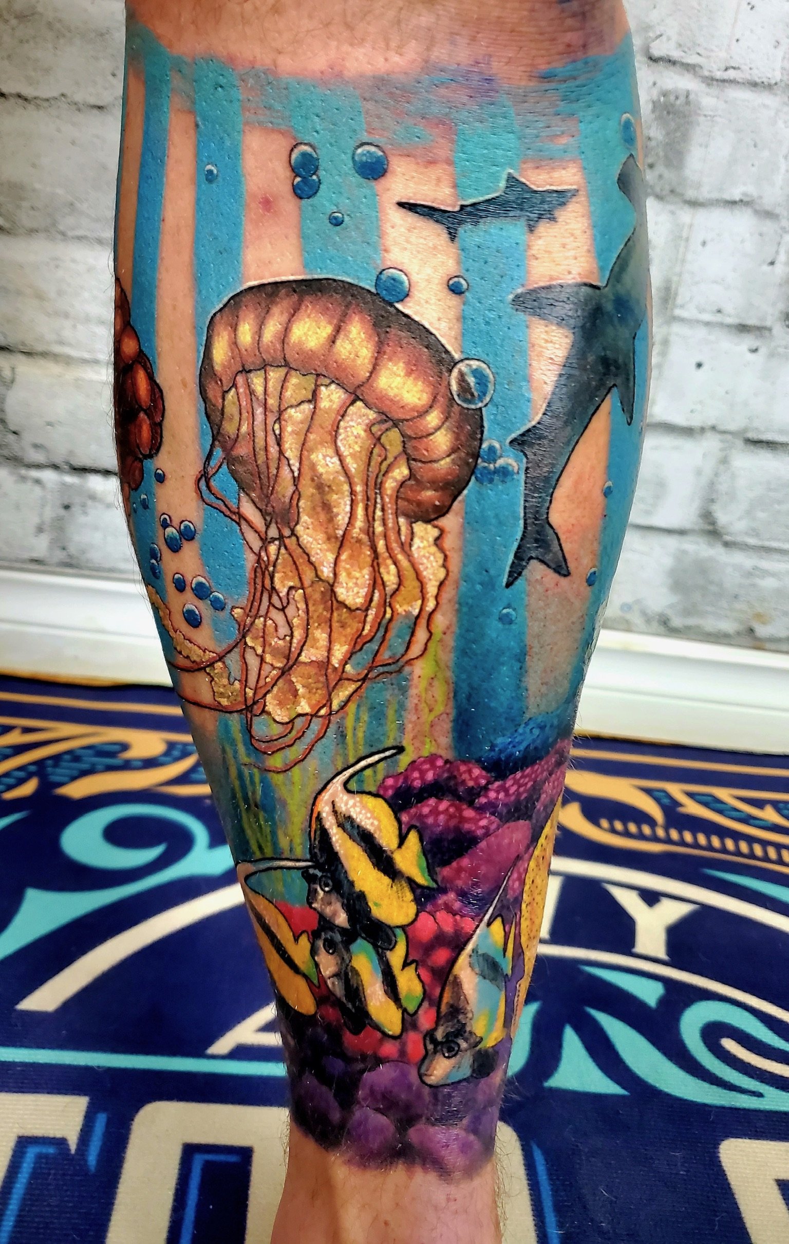 Colorful tattoo sleeve on person's arm featuring underwater scene with jellyfish, sharks, a bee, and other sea creatures.