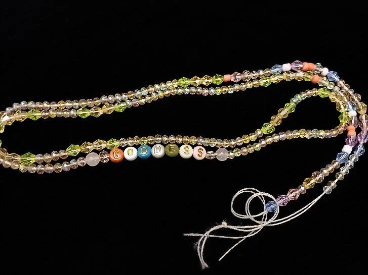 Colorful beaded necklace spelling 'Guess' with a black background.