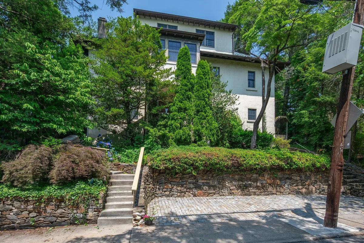 Set above street behind stone retaining walls, with off-street cobblestone parking area at grade, steps rise through terraced garden
