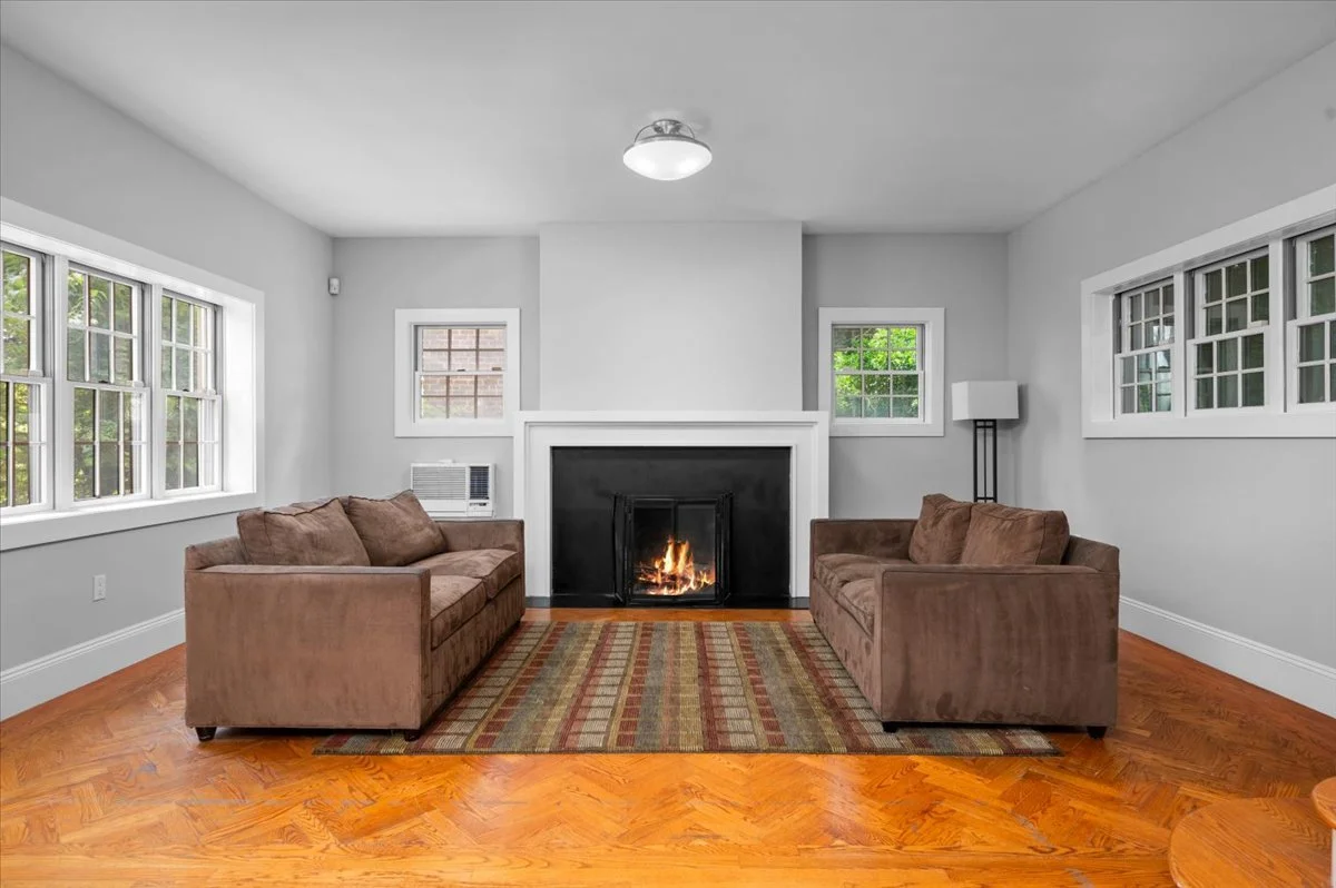 Living room with wood-burning fireplace, oversized picture windows overlooking gardens, Eastern, Western, and Southern exposures, hardwood flooring