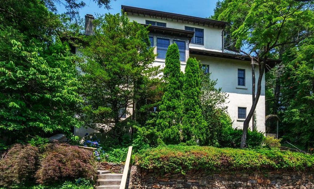 Set above street behind stone retaining walls, cobblestone off-street parking area at grade, steps rise through terraced garden area to entrance