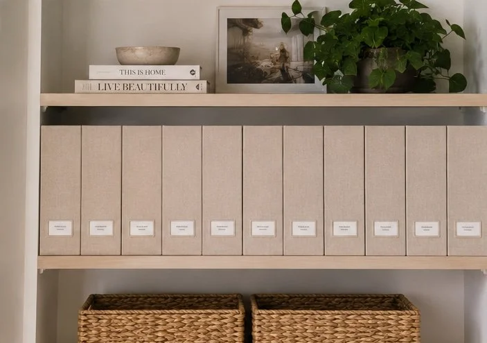 Home organization shelf with beige storage boxes, a framed picture, a green plant, a bowl, and decorative books.