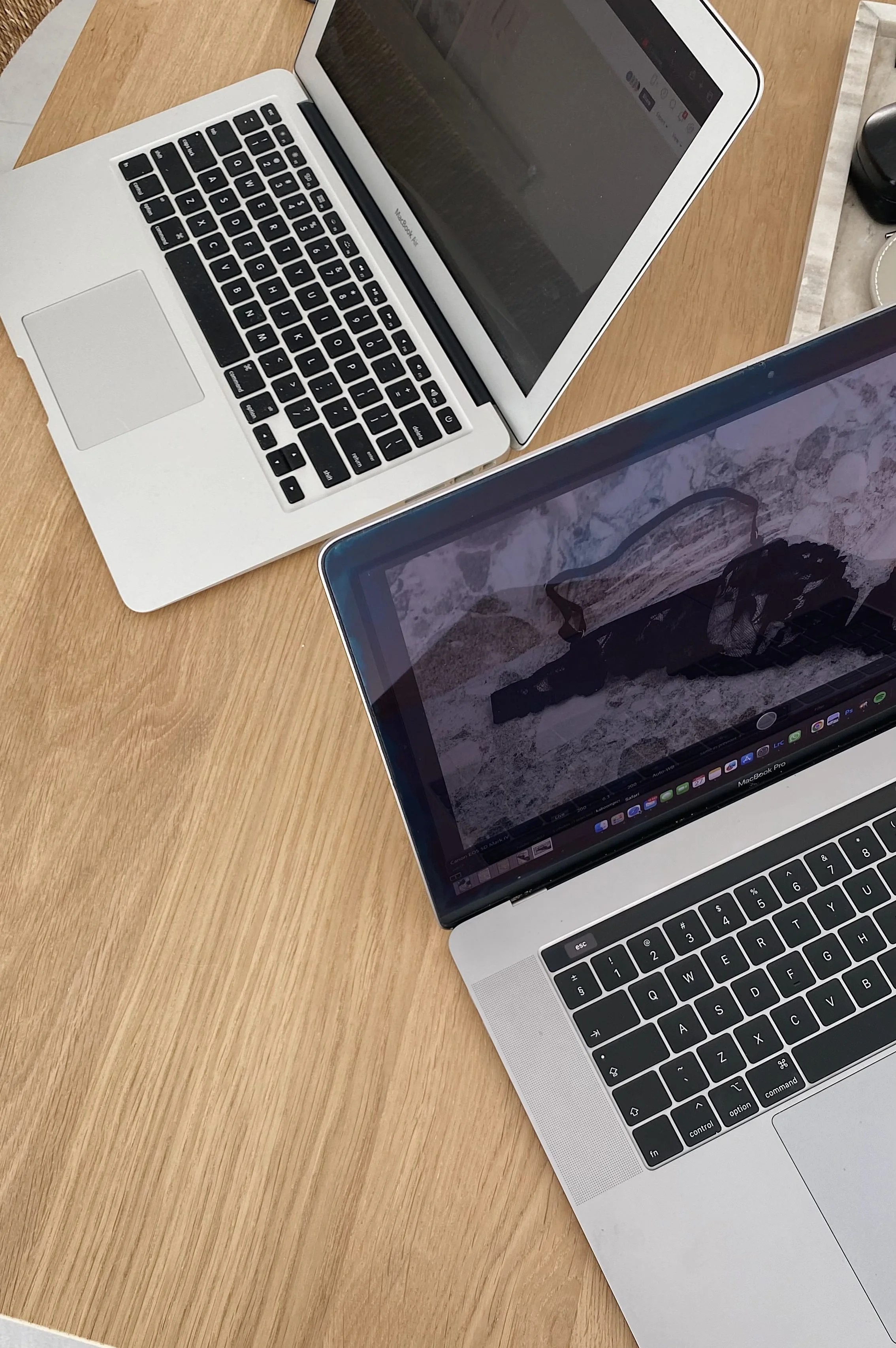 Two laptops on a wooden table, one in the foreground with a mountain and lake wallpaper, and the other in the background with a closed black screen.