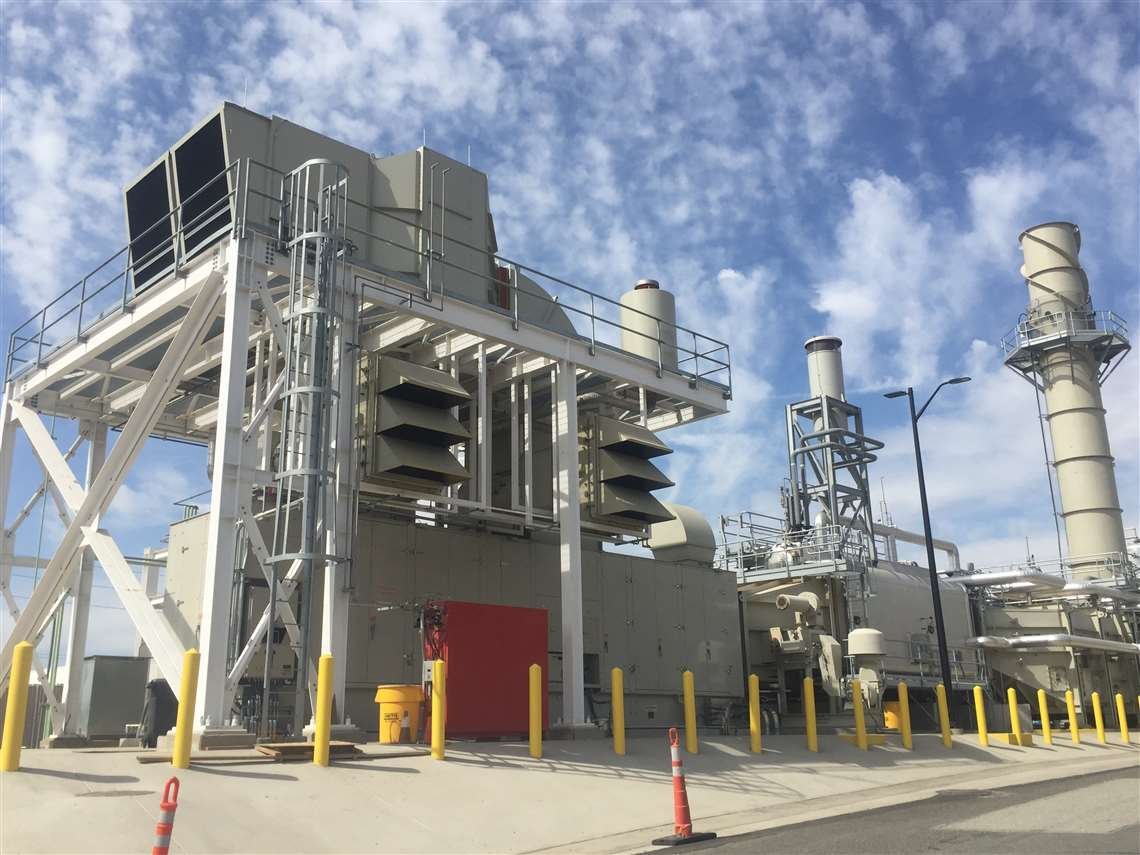 Industrial facility with large equipment, piping, and exhaust stacks under a cloudy sky.