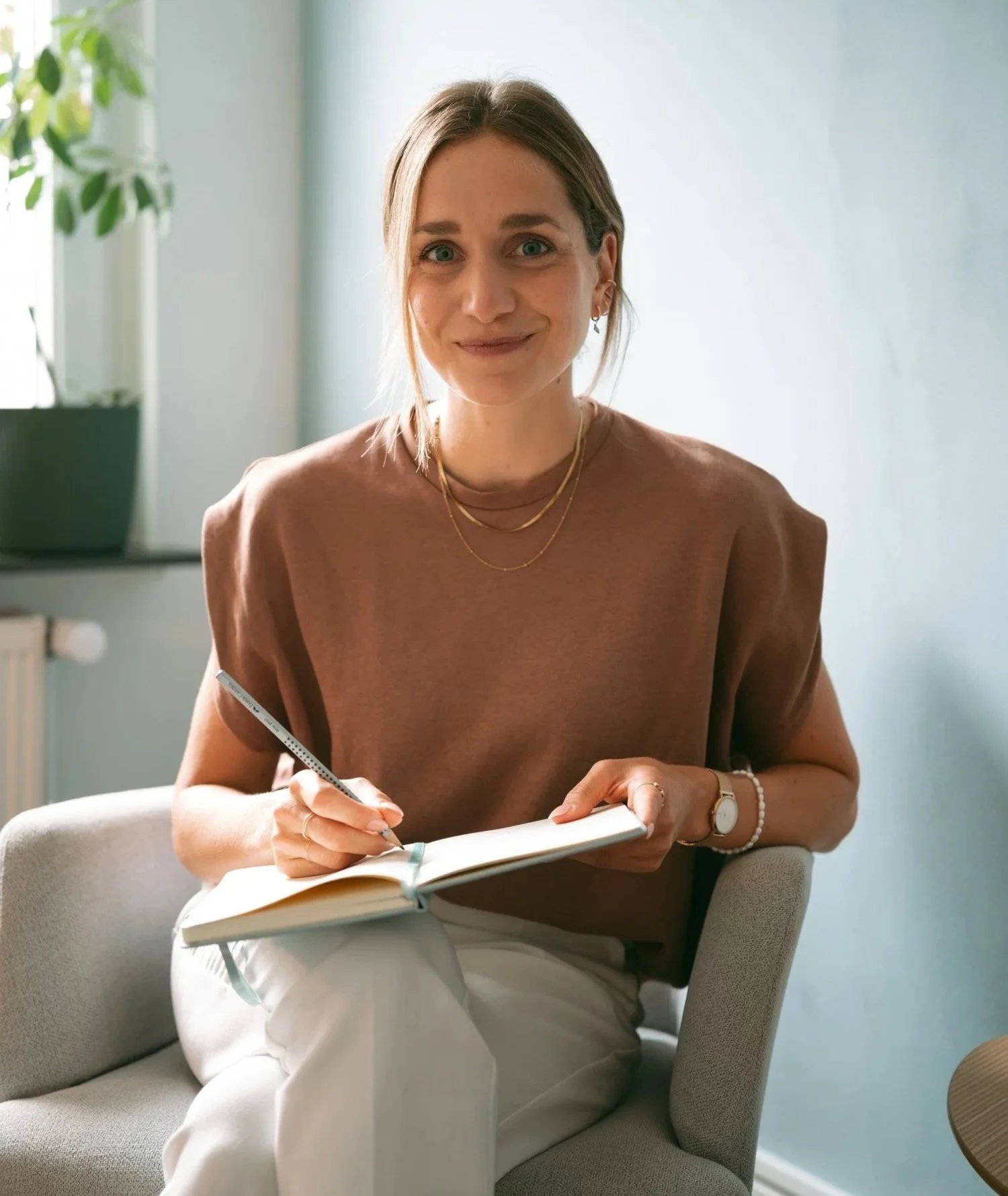 M.Sc. Psych. Hanna Breit sitzt im Büro, lächelt und schreibt in ein Notizbuch.