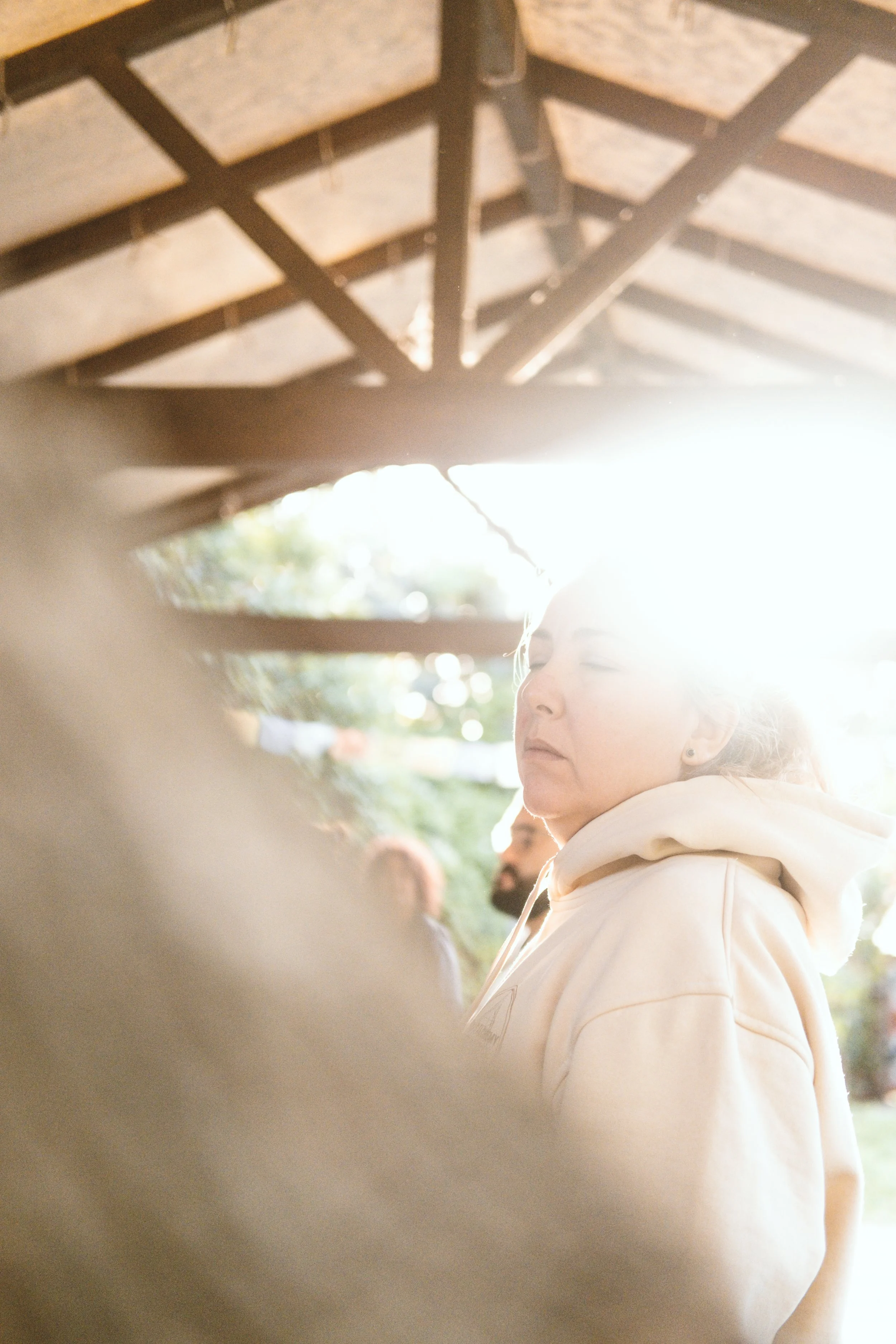 Mujer con sudadera clara, mirándose de perfil, en un entorno exterior con sombra y luz brillante a su alrededor.