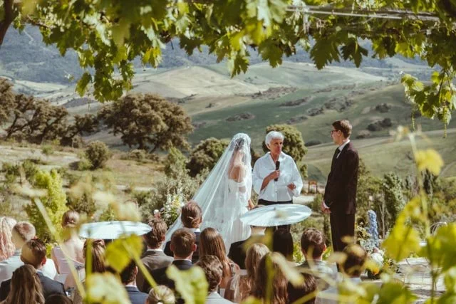 Boda al aire libre con una novia y un novio, una oficiante, y invitados en un paisaje montañoso