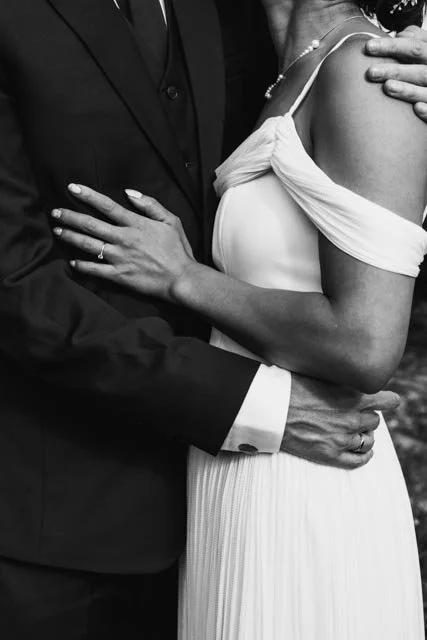 Pareja en boda, ella con vestido blanco y él con traje negro, abrazados.