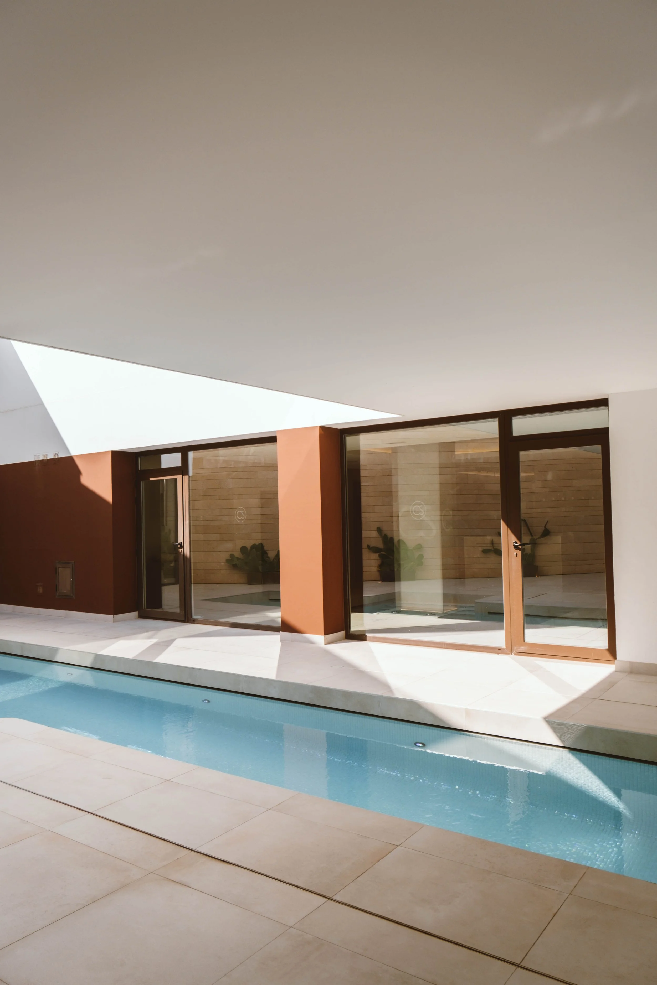 Vista del patio de una casa moderna con una piscina y ventanas grandes que permiten ver el interior con plantas decorativas.