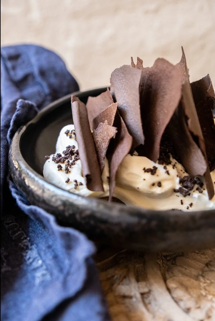 Helado de vainilla en un cuenco con virutas de chocolate y fichas de chocolate, decorado con láminas de chocolate oscuro.