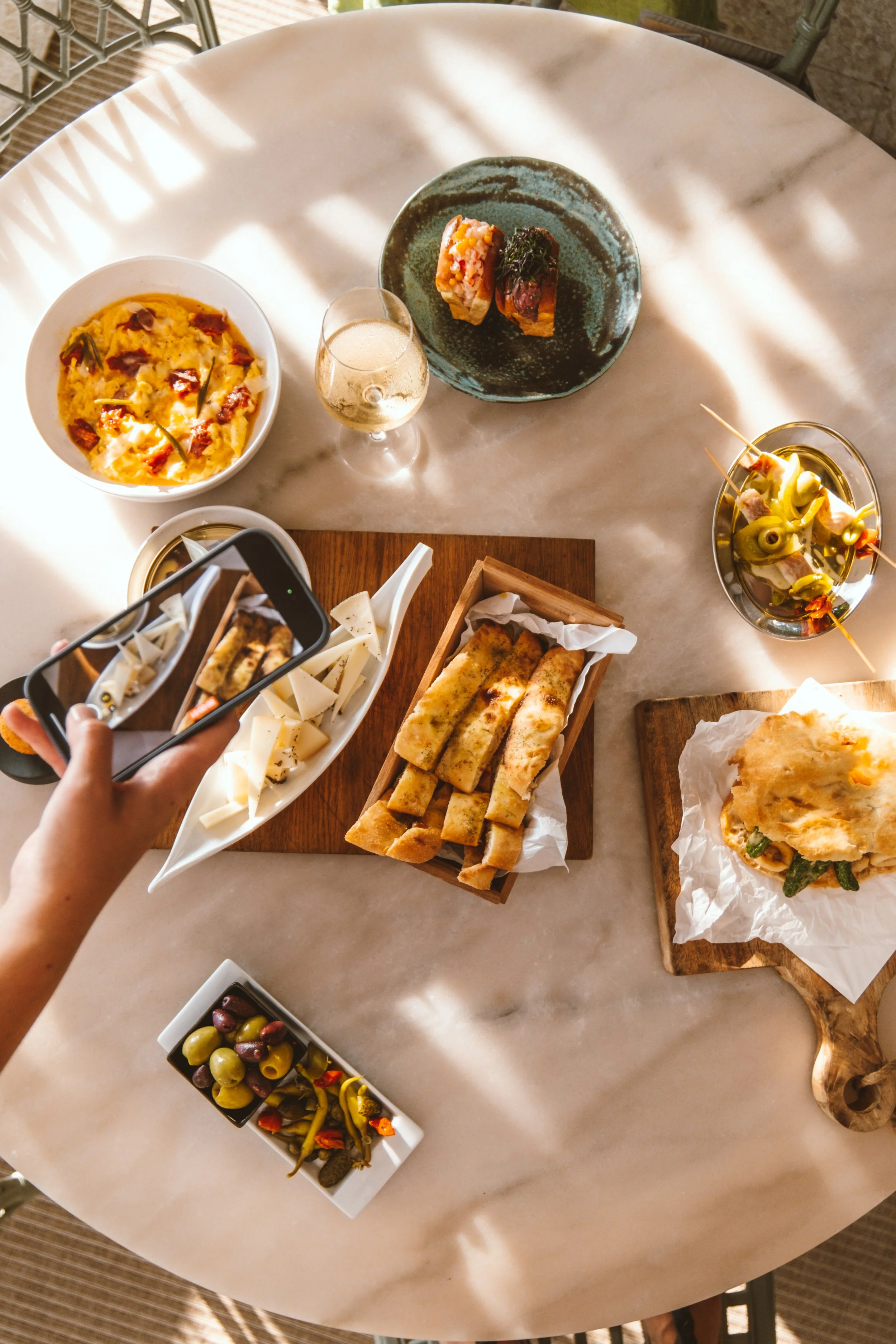 Variedad de platos pequeños y tapas, incluyendo una ensalada en un bol, una bandeja con tagliatelle y un sándwich con verduras, acompañados de aceitunas y vegetales encurtidos, sobre una mesa de mármol.