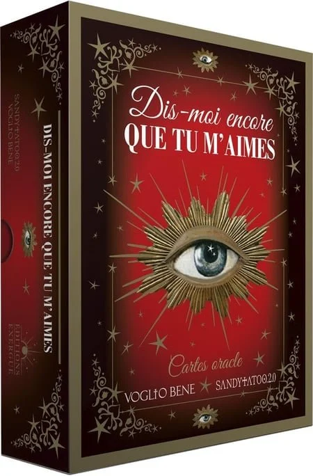 Une boîte de cartes oracles avec un fond rouge et or décoré de motifs étoilés. Le titre en français est "Dis-moi encore que tu m'aimes" et il y a un grand œil central entouré de rayons dorés.