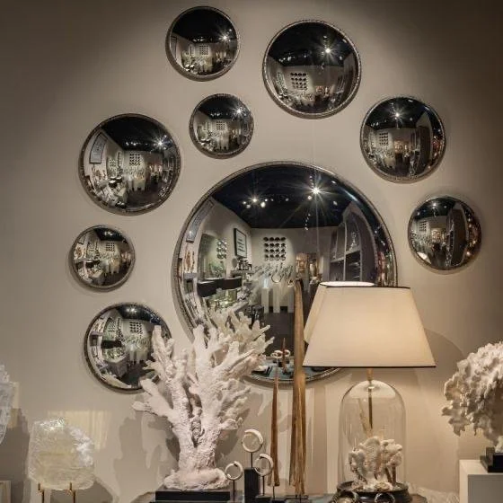 Miroirs ronds de différentes tailles disposés sur un mur, avec un meuble décoratif en dessous, comprenant une lampe et des éléments en forme de corail blanc.