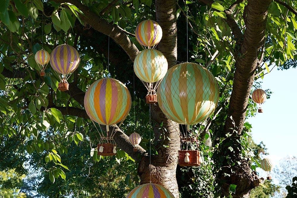 Décor suspendu de ballons en forme de montgolfières en surface d'arbre avec feuilles vertes.