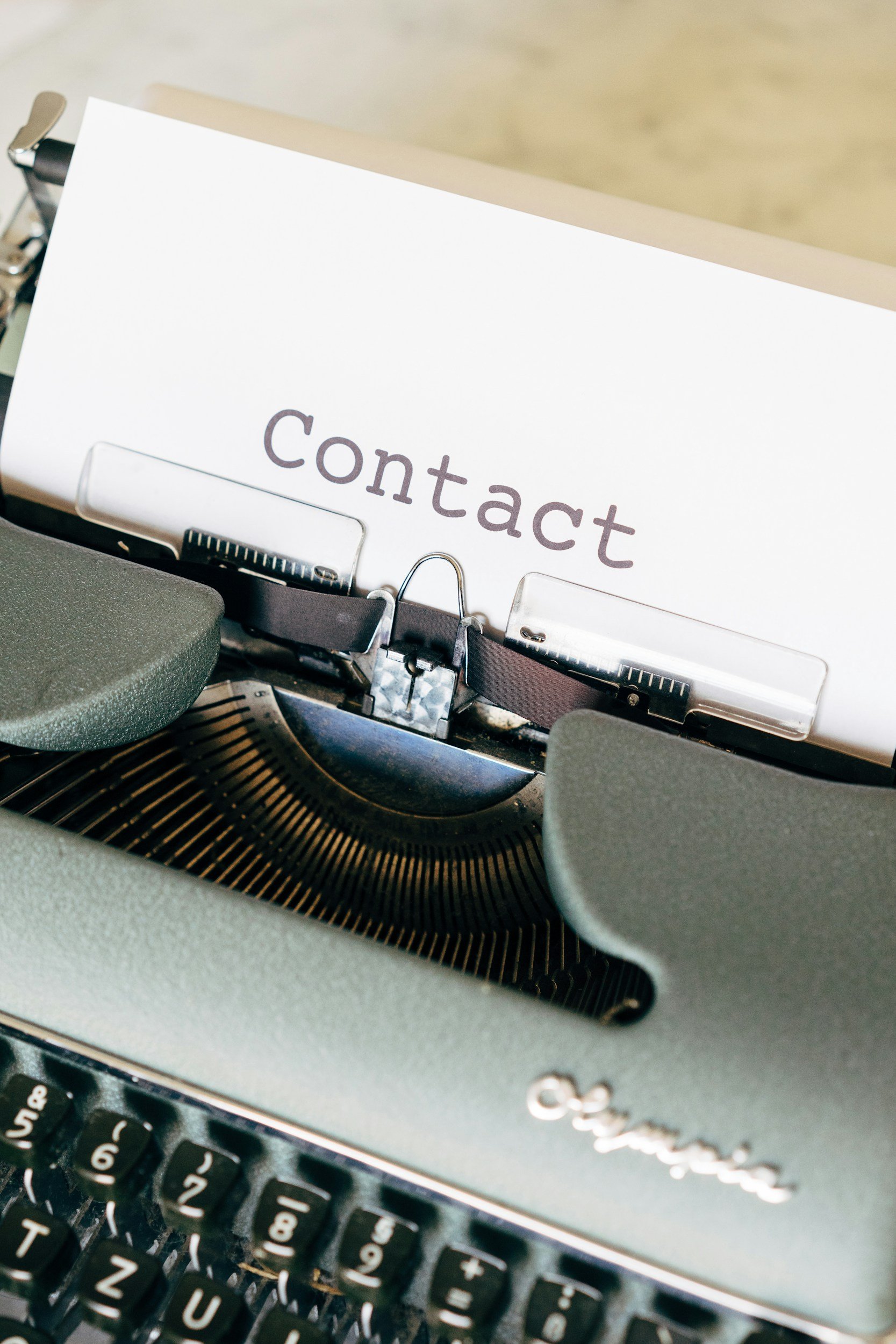 Close-up of a vintage typewriter with a paper inserted, partially showing the word 'Contact' typed on it.