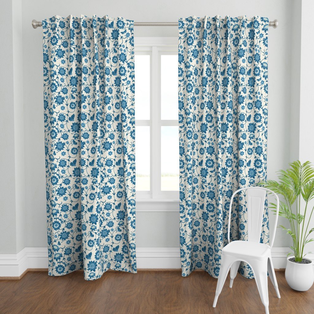Blue and white floral patterned curtains hanging in front of a window, with a white chair and a potted green plant nearby.