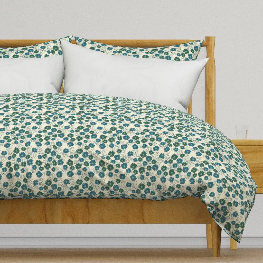 A neatly made bed with a wooden frame, featuring a floral bedspread with green and blue flowers, white pillows, and a plain white wall in the background.
