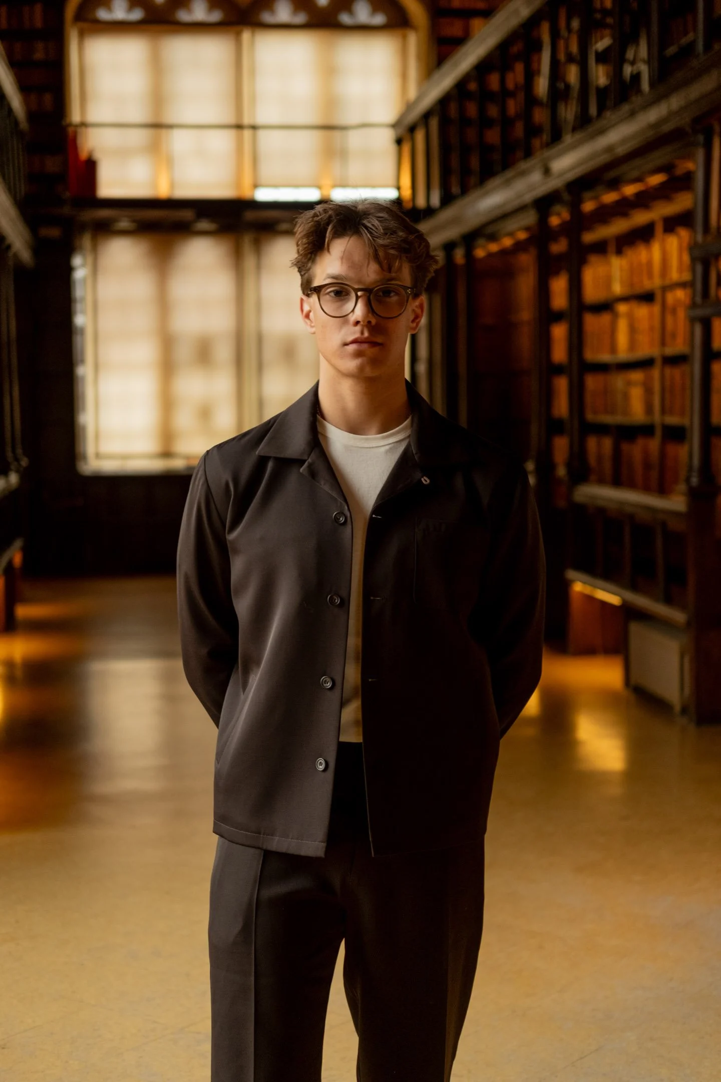 A man wearing clothing by Kenny Ryder in the Duke Humfrey's Library, Oxford. Behind is a library with old books at the University of Oxford.