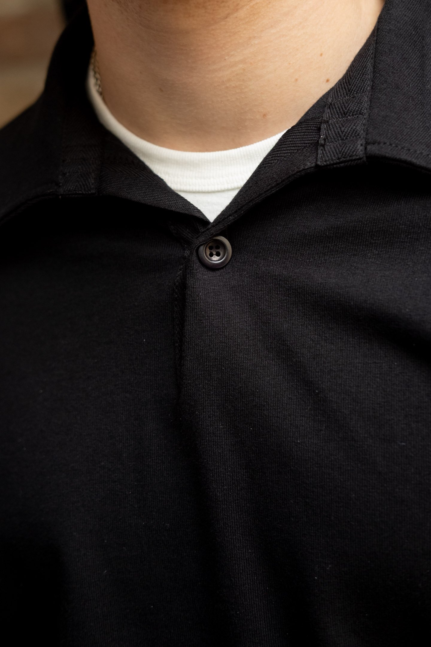A close-up of a man's neck, showing the details on a white Allevol t-shirt and a black Conkers rugby top on top.