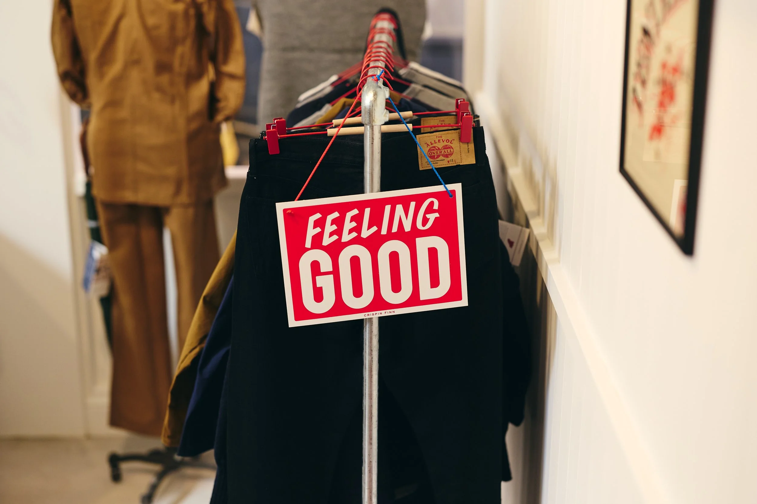 Clothing rack with pants and a sign that says 'Feeling Good' in a store.