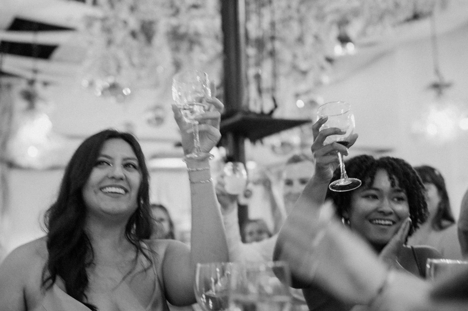 Two women smiling and raising glasses during a celebration in a decorated indoor setting.