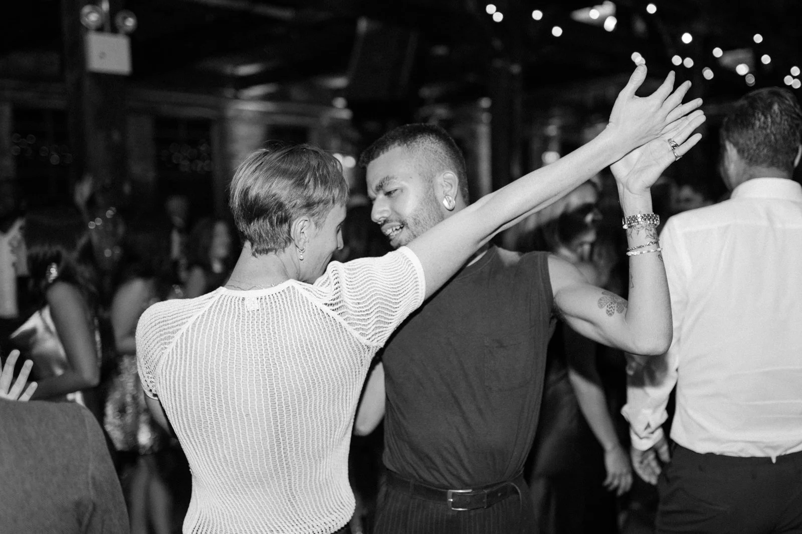 Two people dancing closely at a social gathering, with other guests visible in the background.