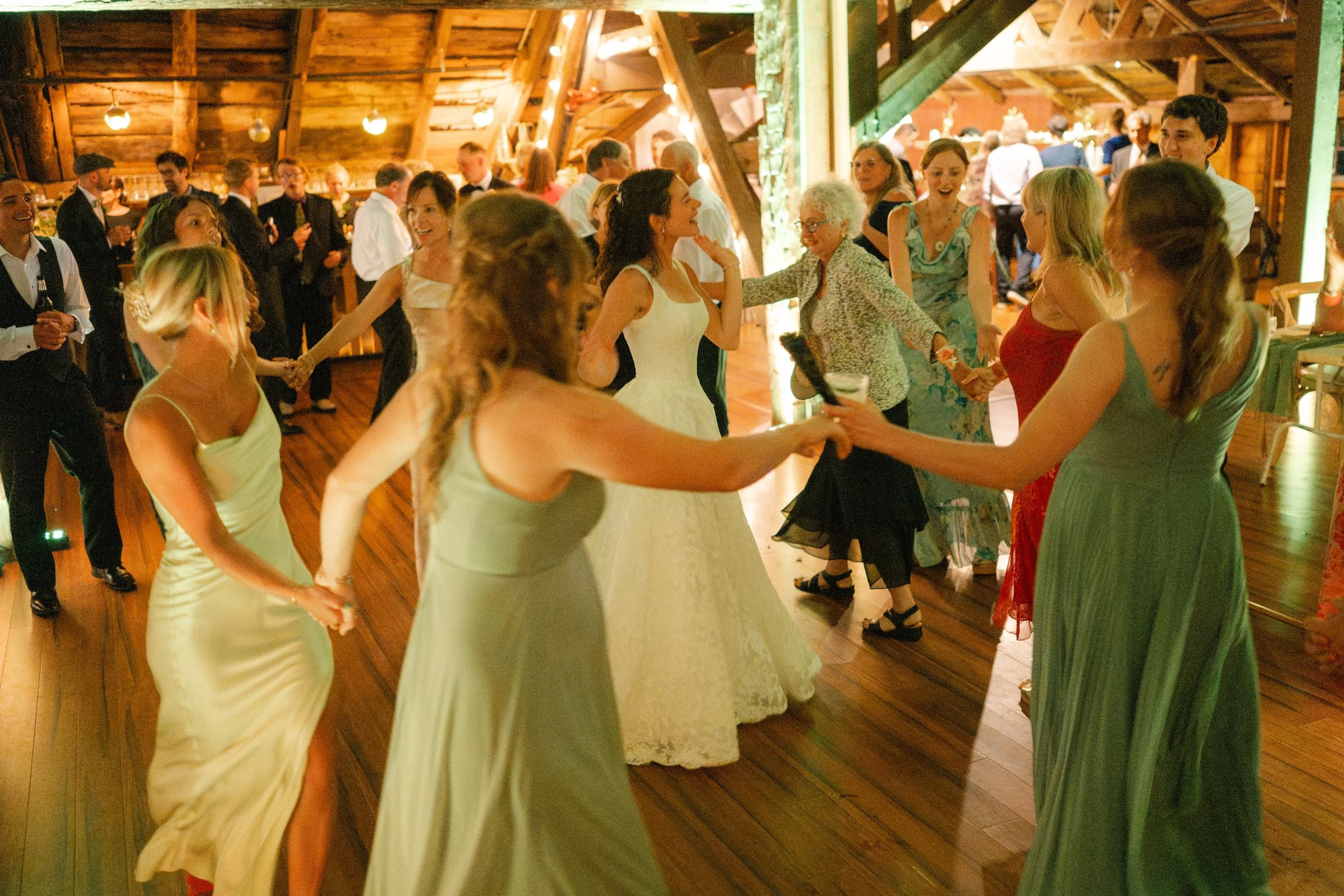 People dancing in a rustic wooden hall at a wedding celebration.