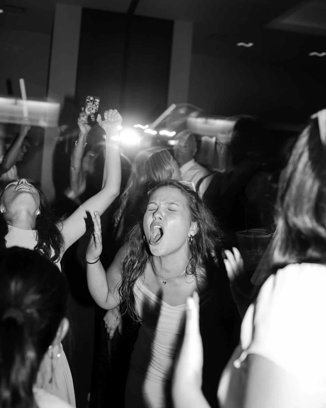 People dancing and singing passionately at a lively party or celebration, with energetic expressions and raised hands.