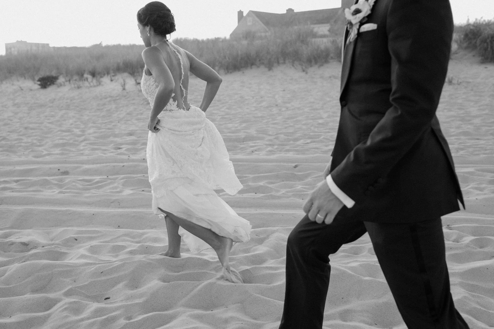 A bride in a wedding dress and a groom in a suit walking on the beach.