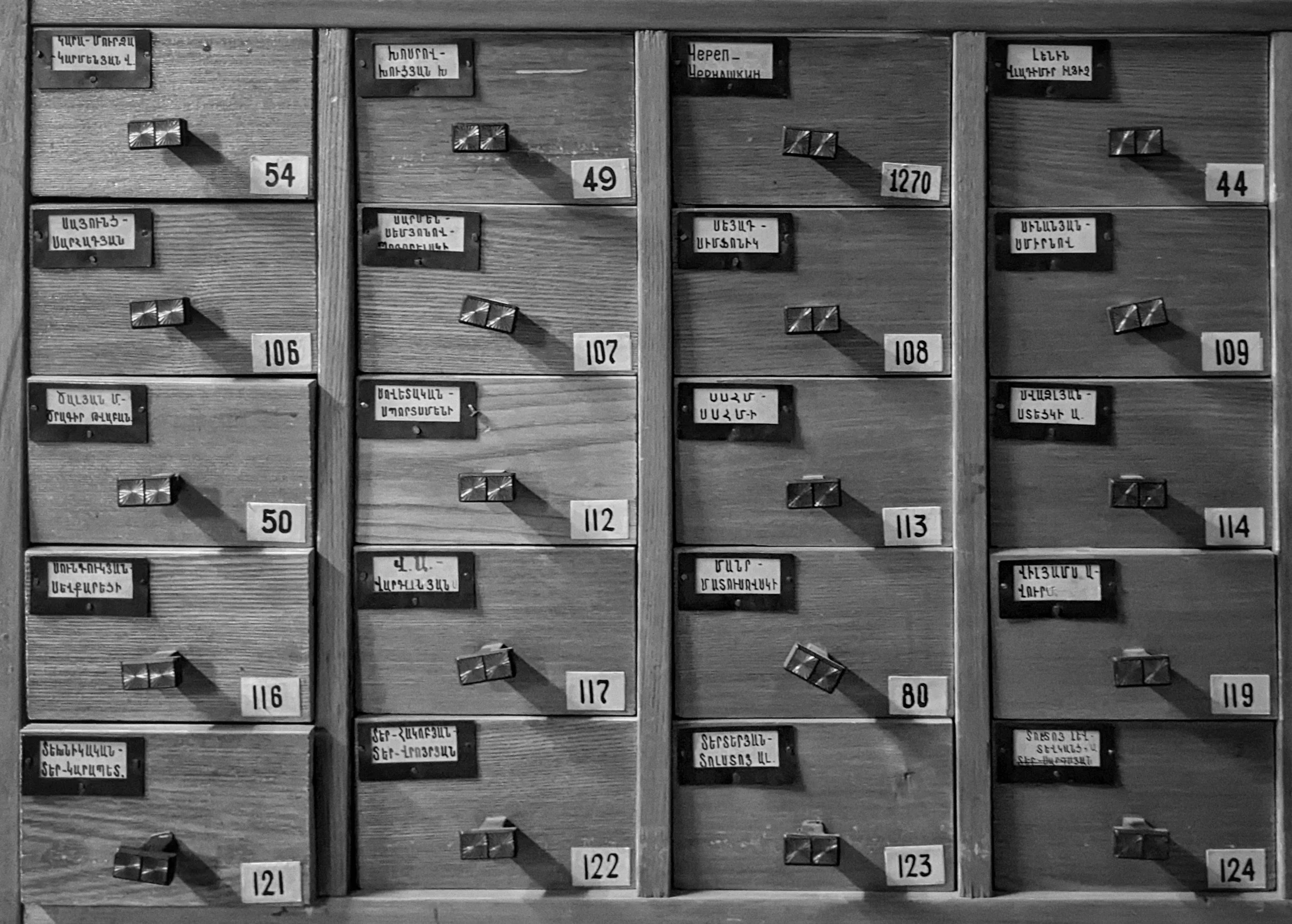 A black and white photograph of wooden drawers with metal handles and labels written in Armenian, each drawer numbered, arranged in a grid pattern.