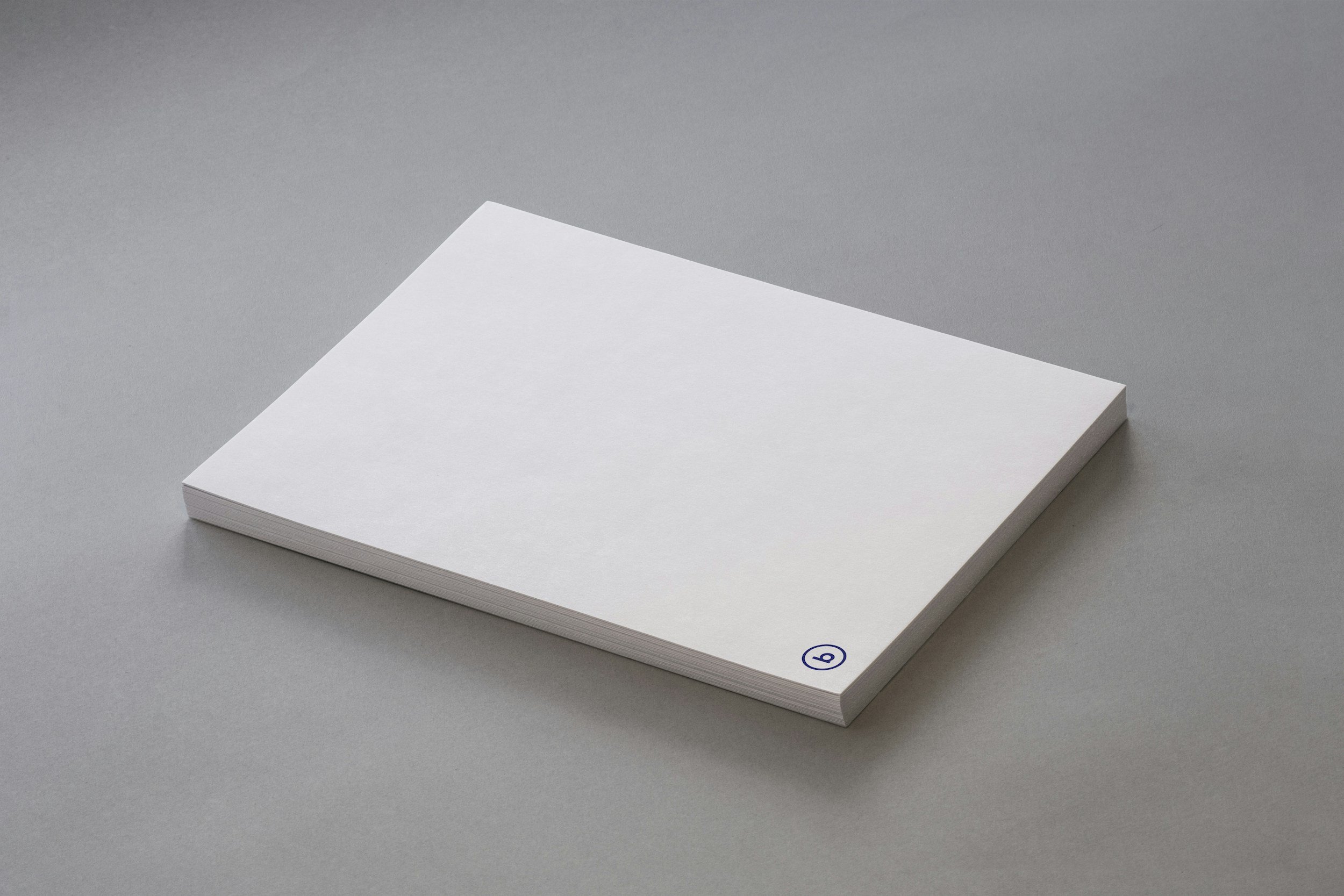 A stack of white paper with a small blue circle at the bottom right corner on a gray surface.