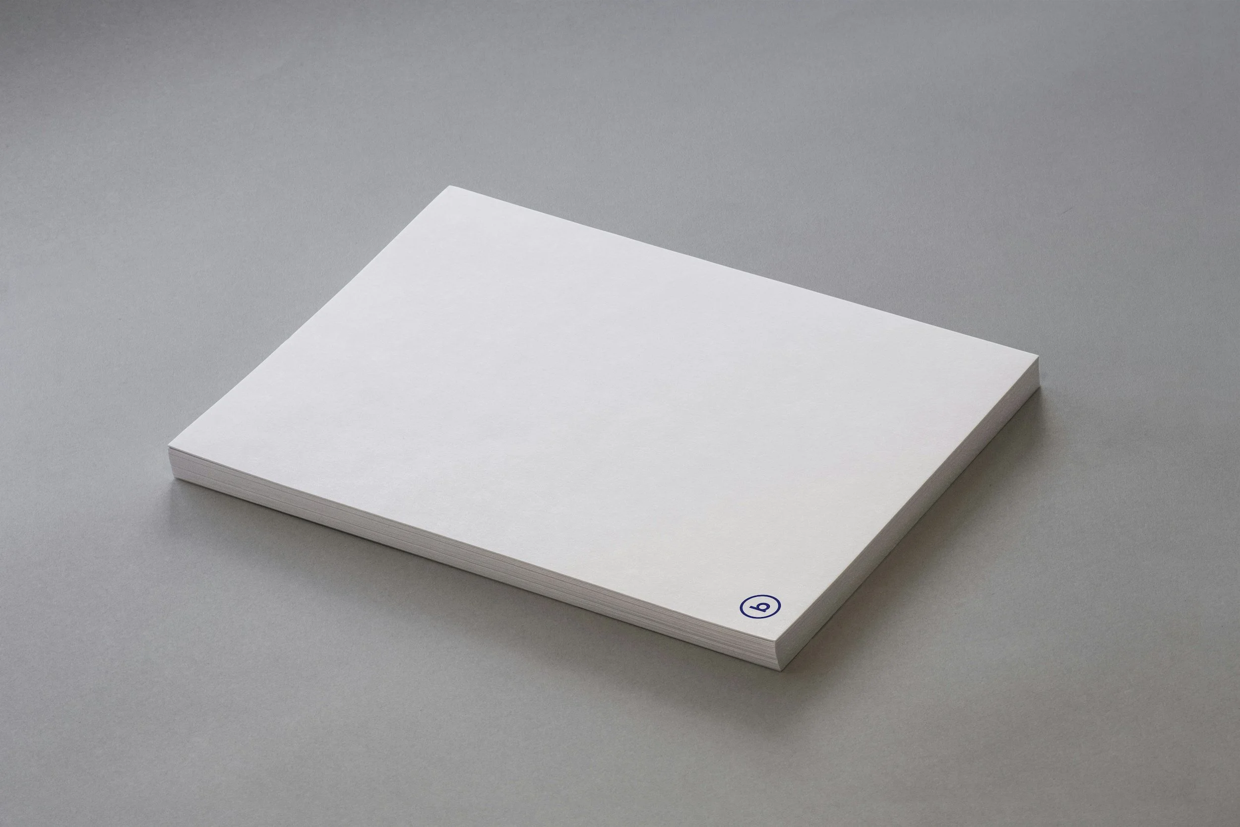 A stack of white paper sheets on a gray surface with a small blue logo or emblem near the bottom right corner.