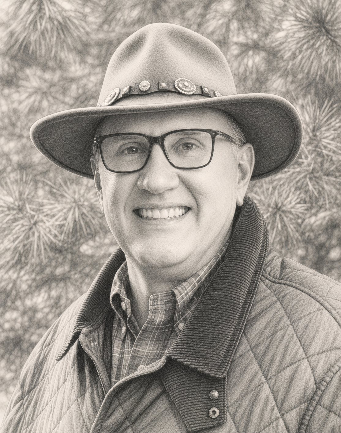 A smiling man wearing glasses, a wide-brimmed hat with decorative elements, a plaid shirt, and a quilted jacket, outdoors with trees in the background.