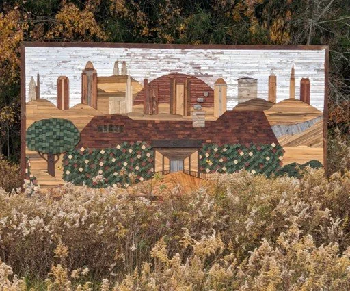 A mural depicting a city skyline with buildings, a bridge, trees, and hills, painted with various shades of brown, green, and gray.