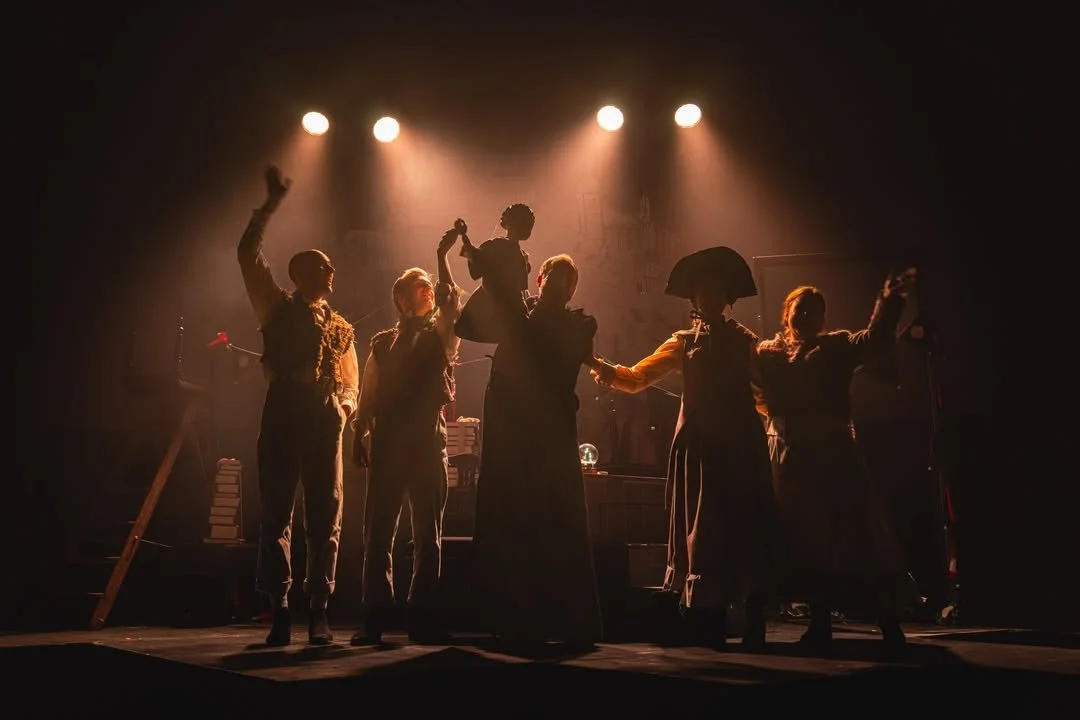 People holding hands and one person lifting another on stage, illuminated by stage lights.