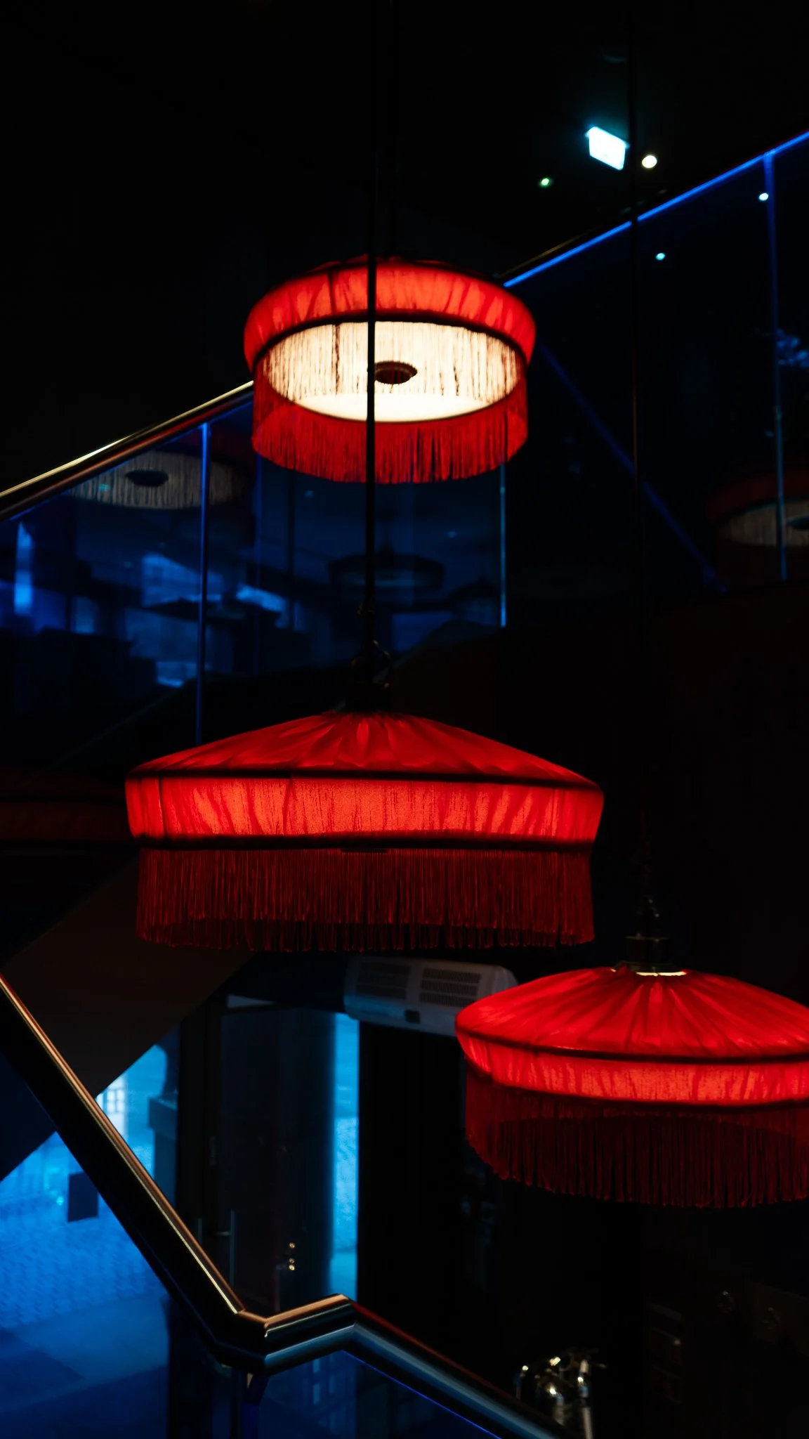 Multiple red hanging lamps with fringes, reflected on a mirror, illuminated in a dark room.
