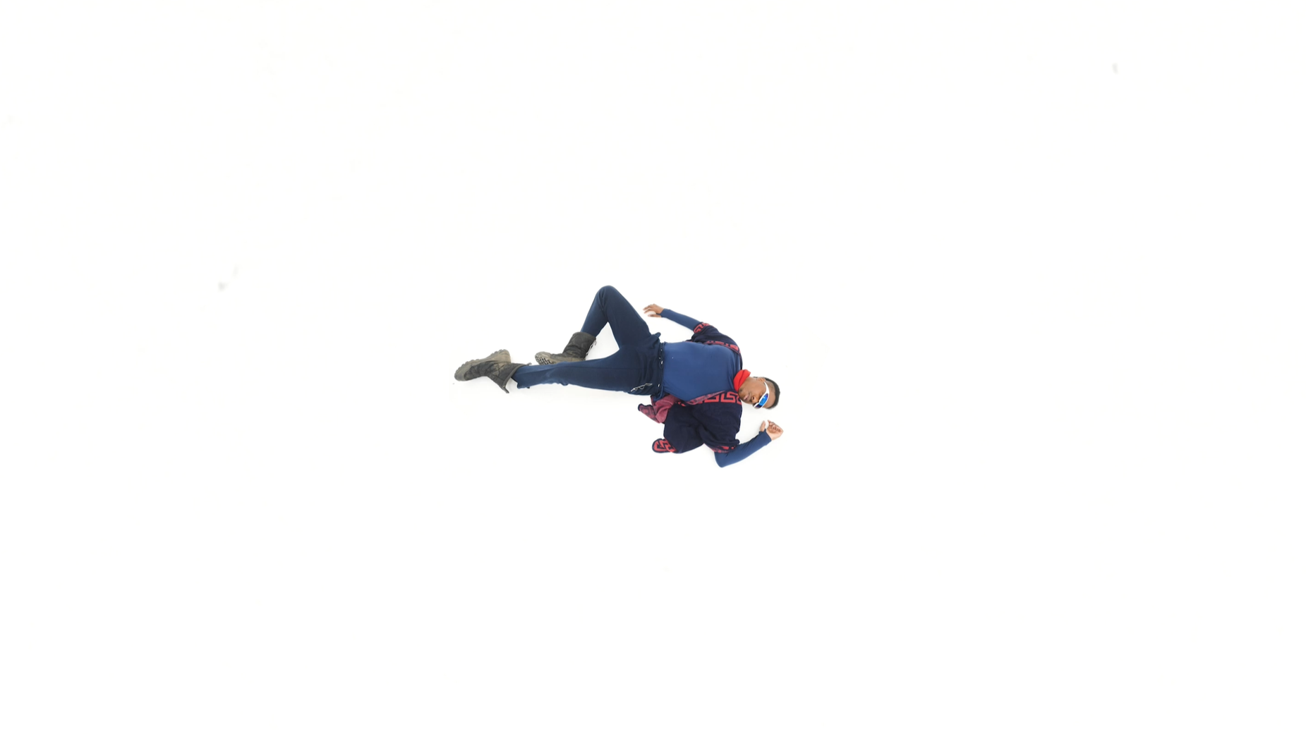 Person lying on the snow, dressed in winter attire, including a mask and sunglasses.
